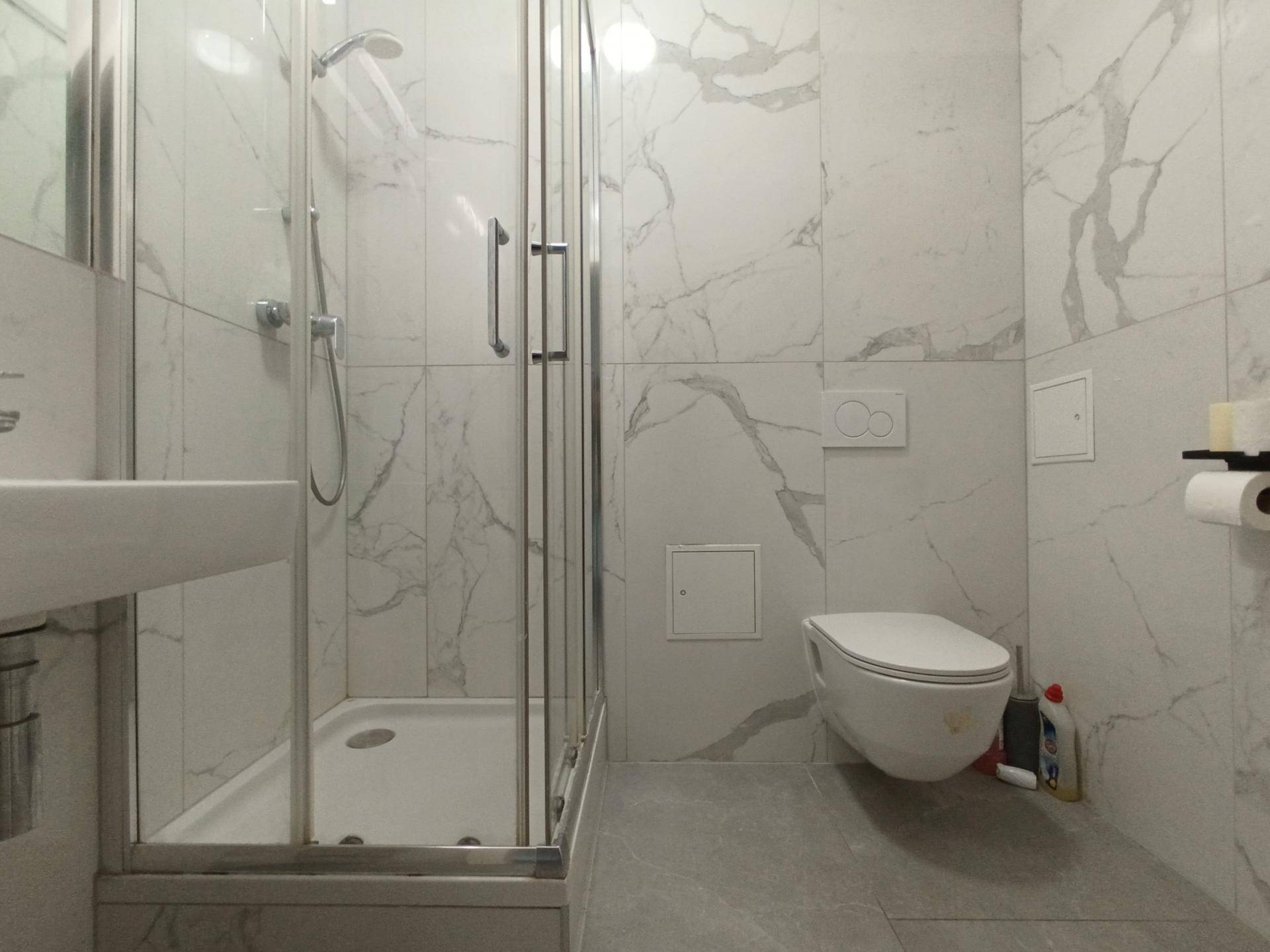 Modernes Badezimmer mit Duschkabine, wandhängendem WC und eleganten Marmorfliesen.