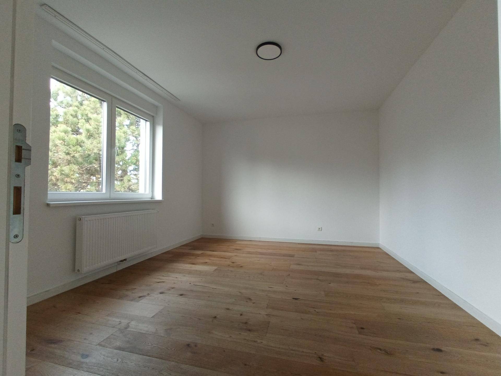 Geräumiges Schlafzimmer mit Holzboden und einem großen Fenster mit Blick ins Grüne.