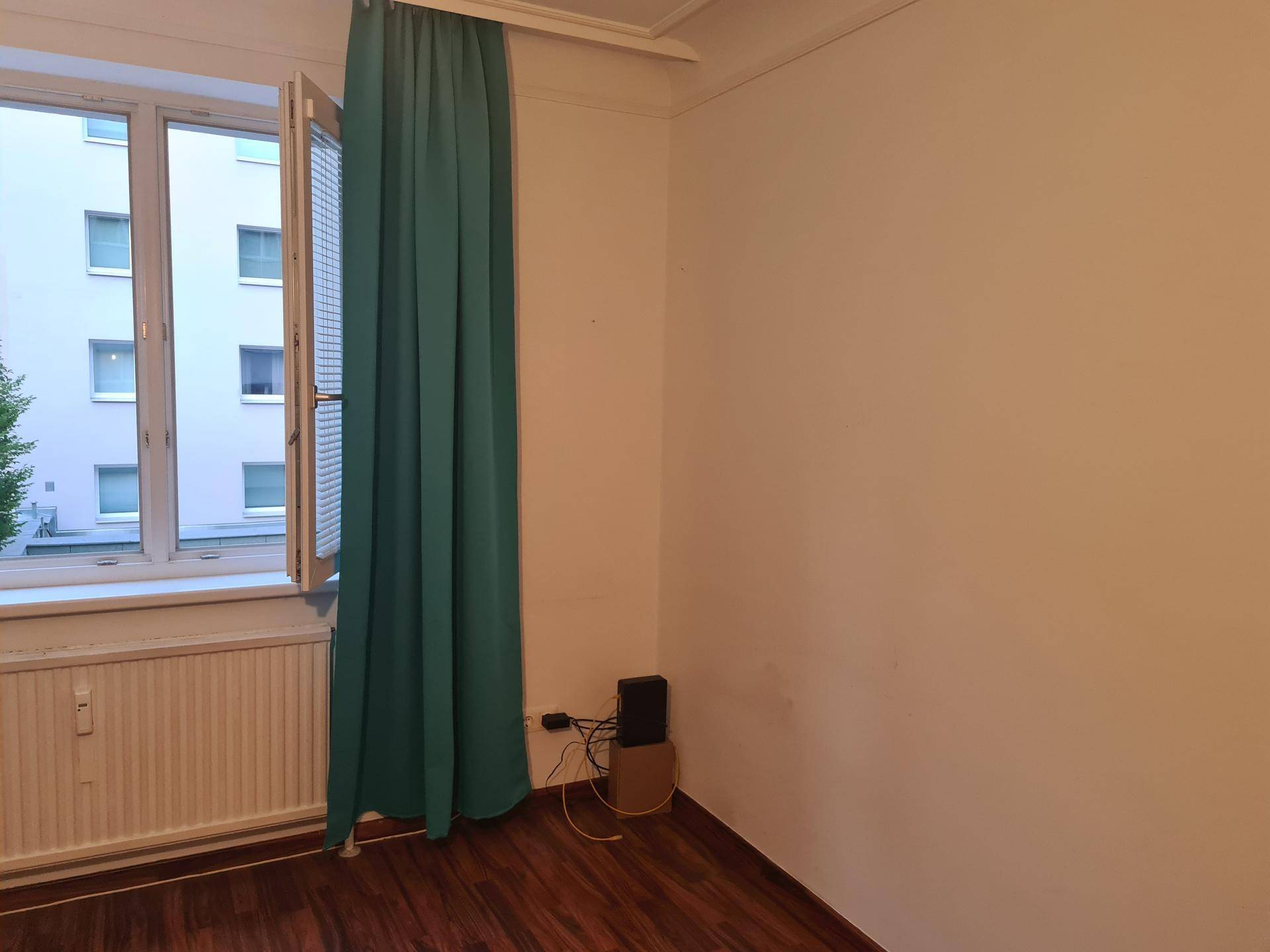 Heller Raum mit Holzboden, großem Fenster und einem Heizkörper unter dem Fenster.