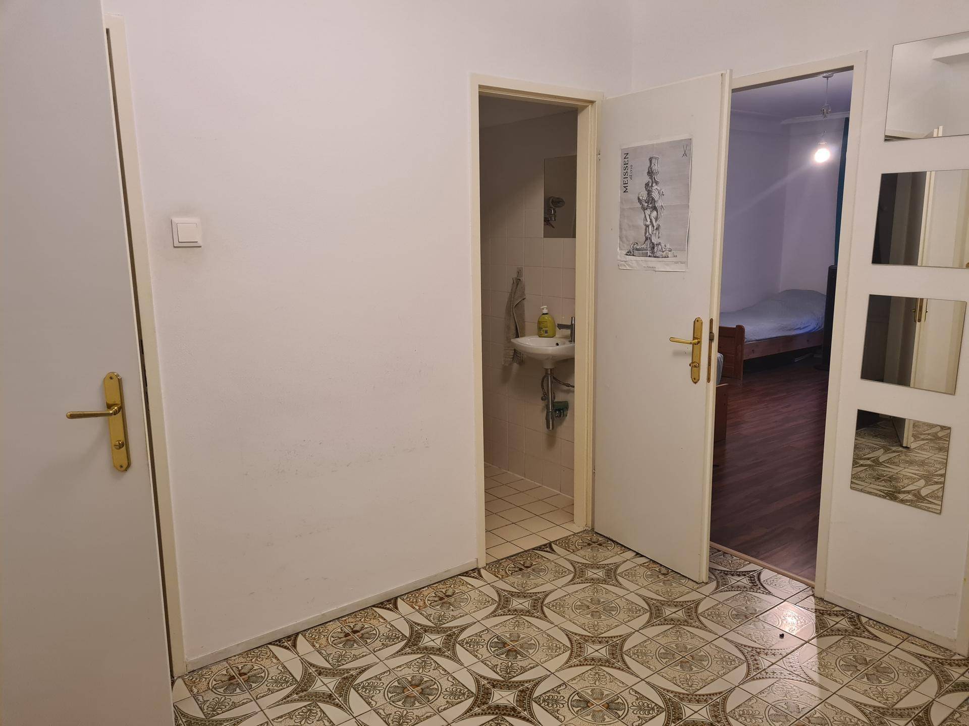 Flur mit gemusterten Fliesen, der zu einem WC und einem weiteren Zimmer führt.