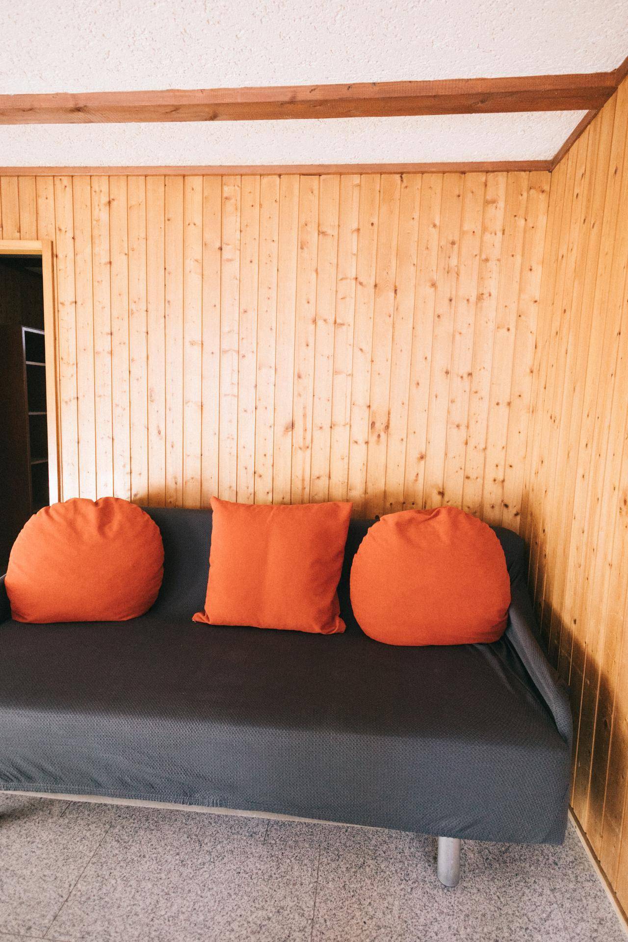 Gemütliches Wohnzimmer mit Sofa und orangefarbenen Kissen, umgeben von Holzvertäfelung.