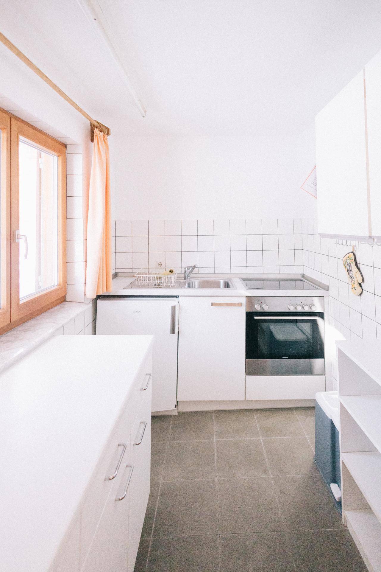Funktionale Küche mit weißen Schränken, integriertem Kühlschrank und Fenster, hell und sauber.
