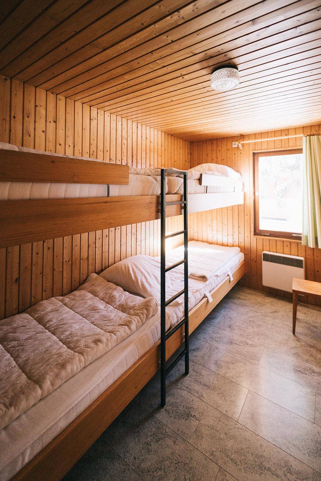 Schlafzimmer mit Etagenbetten und Holzvertäfelung, ideal für Gäste oder Kinder, hell durch das Fenster.