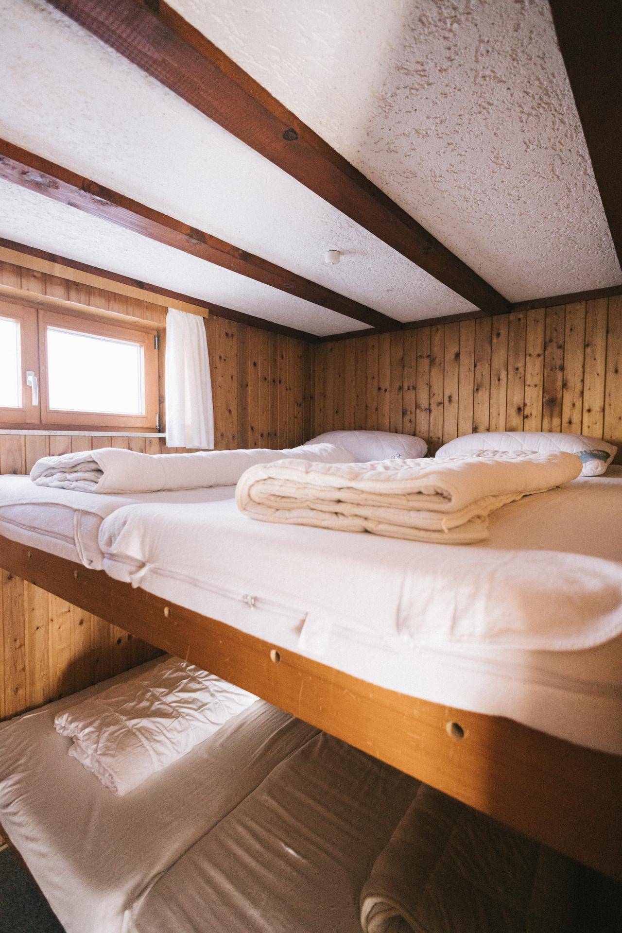 Schlafzimmer mit Etagenbetten und Holzverkleidung, hell und einfach eingerichtet, mit Holzbalken.