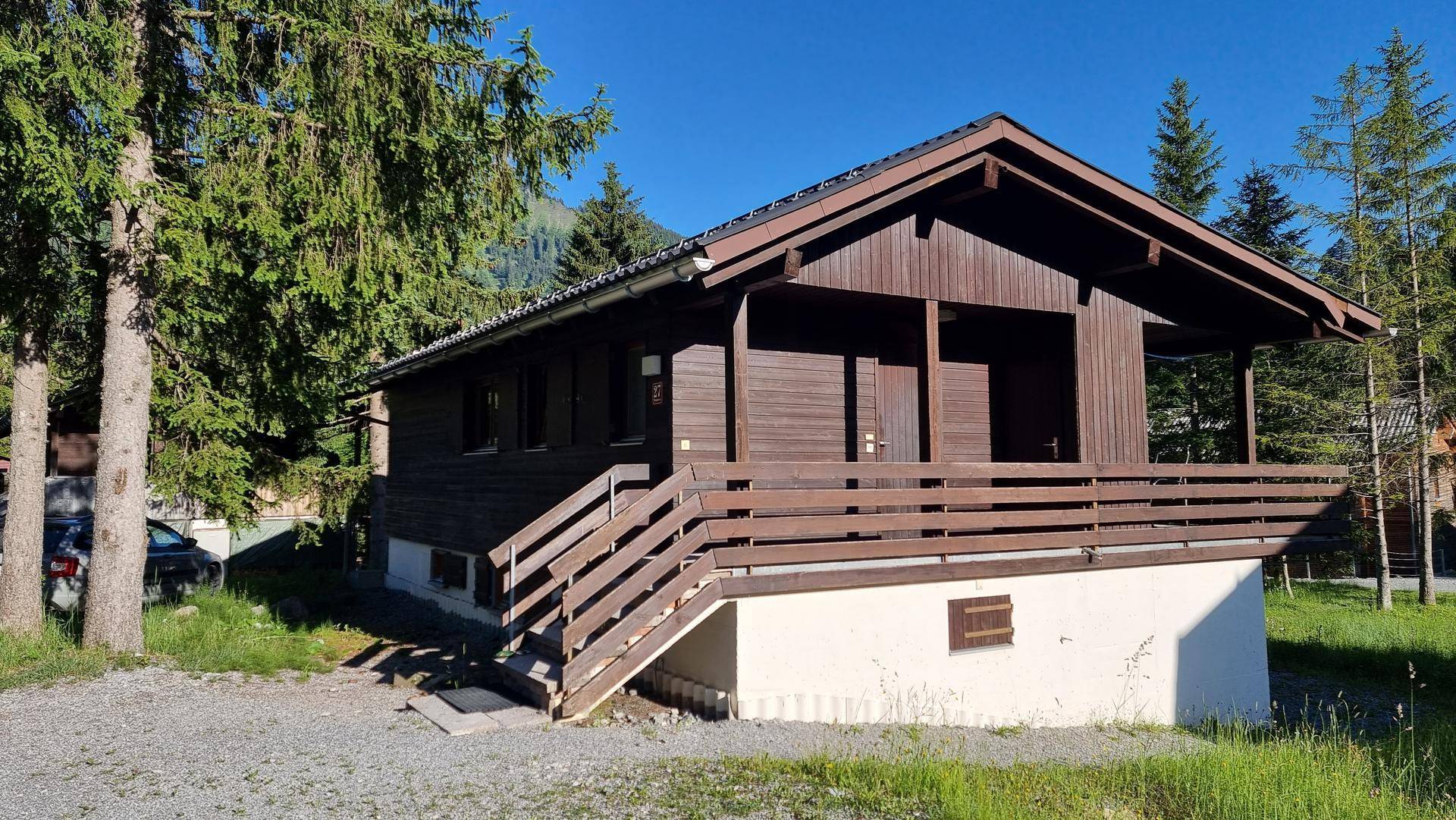 Rustikales Holzhaus mit Satteldach und umlaufendem Balkon in alpiner Landschaft, umgeben von Bäumen.