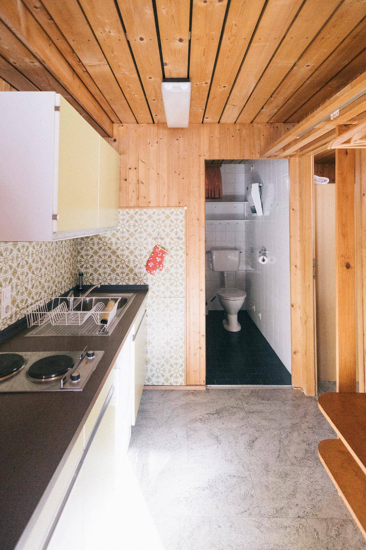 Kleine Küche mit gelben Oberschränken und Zugang zu einem separaten WC, funktional eingerichtet.