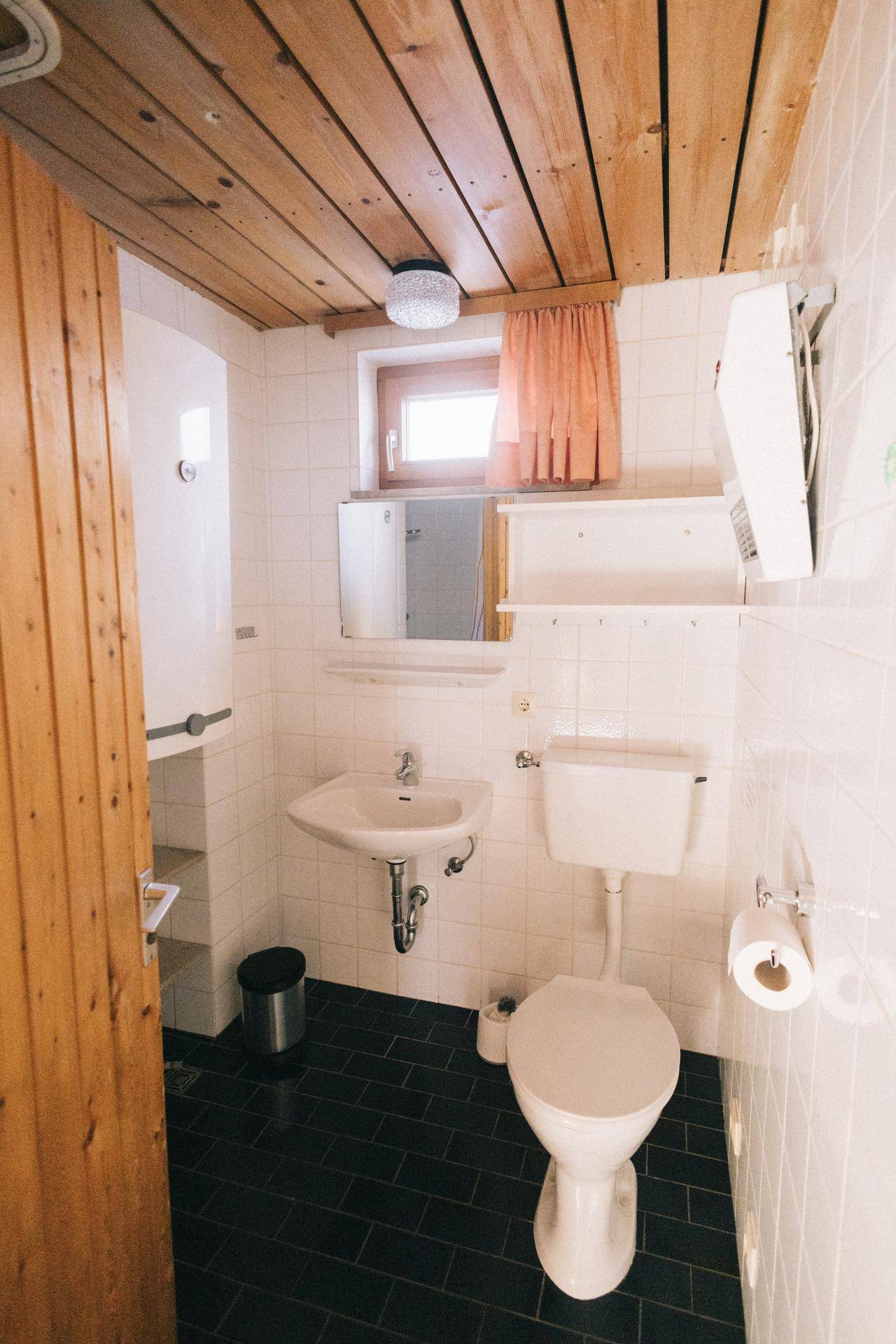 Einfaches WC mit Waschbecken und Fenster, komplett gefliest in Weiß und Dunkelblau, sauber und hell.