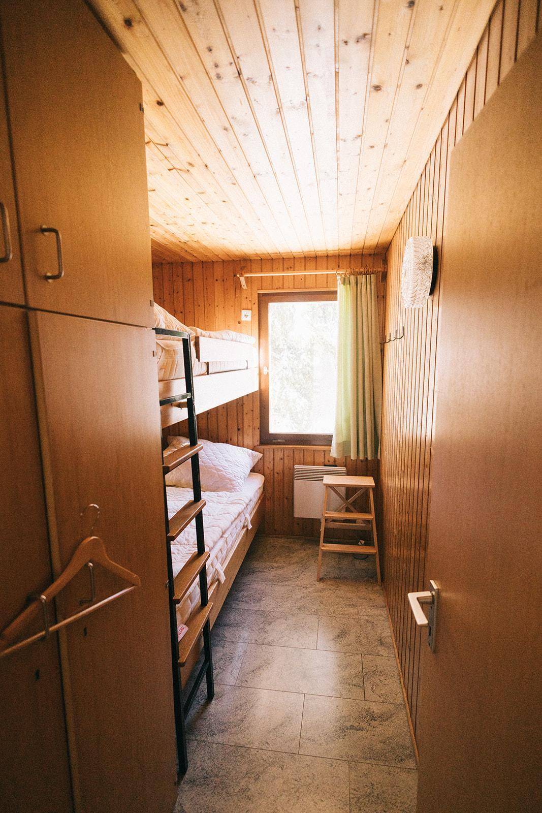 Schmaler Schlafbereich mit Etagenbett und Holzverkleidung, praktisch eingerichtet mit Schrank.