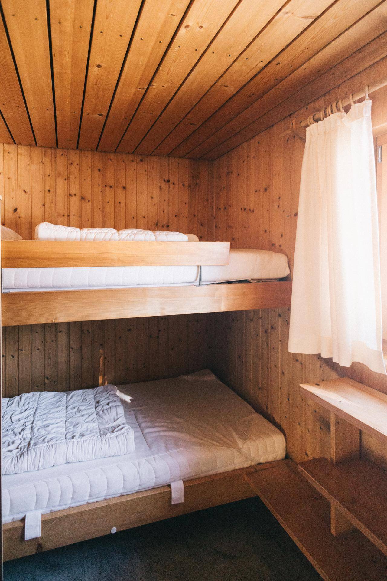 Schlafzimmer mit Etagenbetten und Holzverkleidung, hell und funktional eingerichtet, mit Fenster.