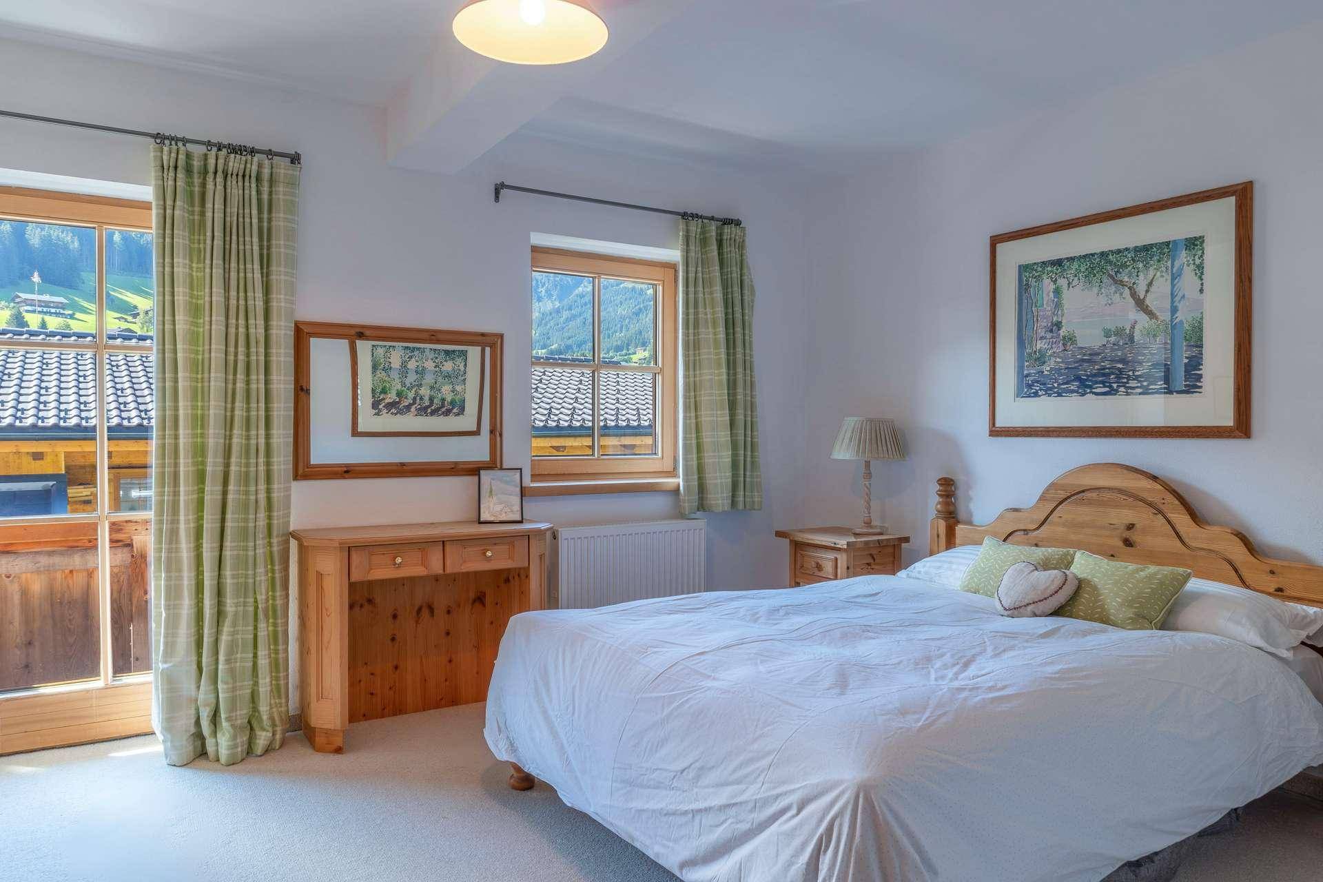 Komfortables Schlafzimmer mit Doppelbett, Holzmöbeln und Zugang zu einem französischen Balkon.