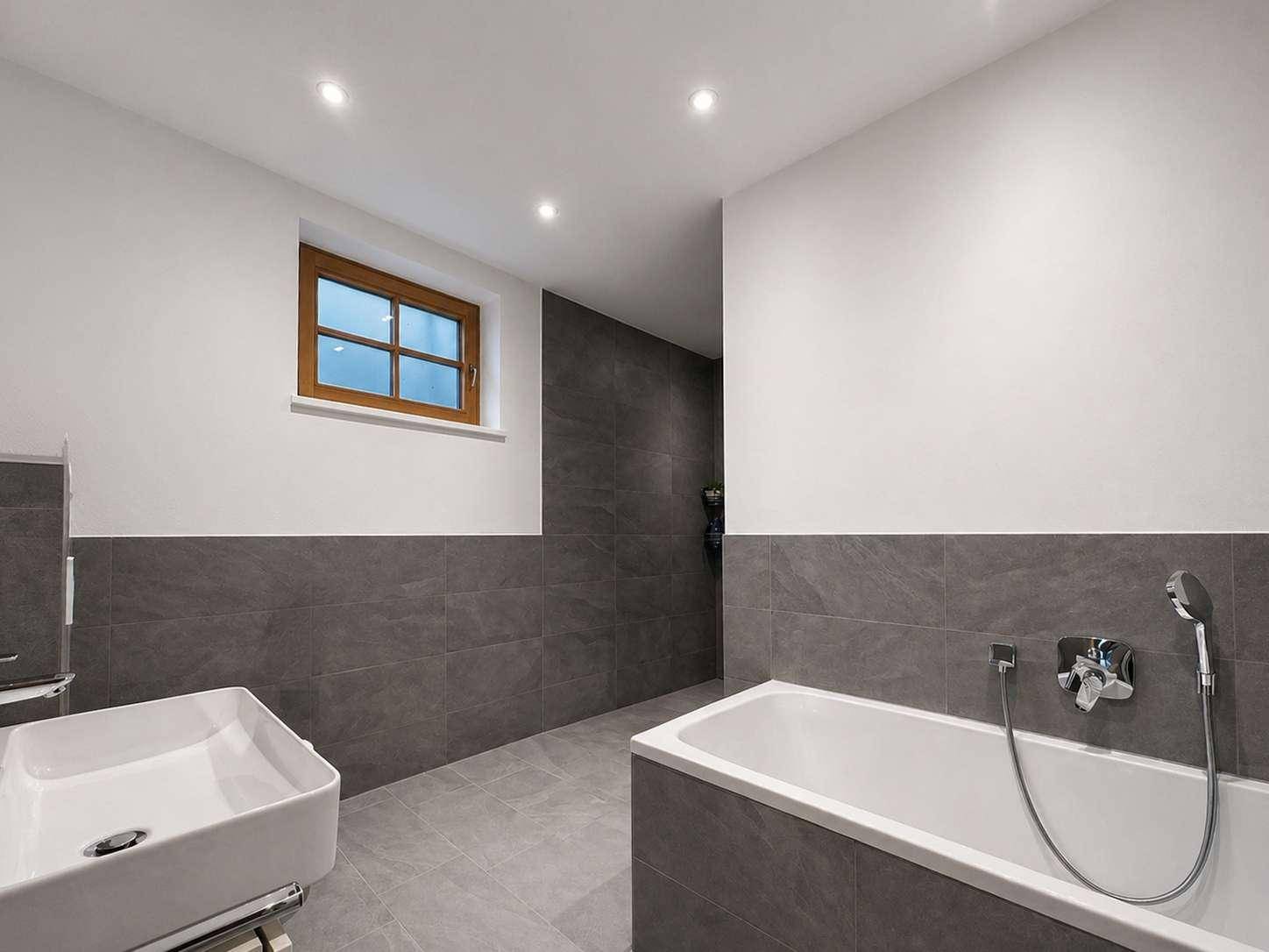 Modernes Badezimmer mit Badewanne, Waschbecken und eleganten grauen Fliesen.