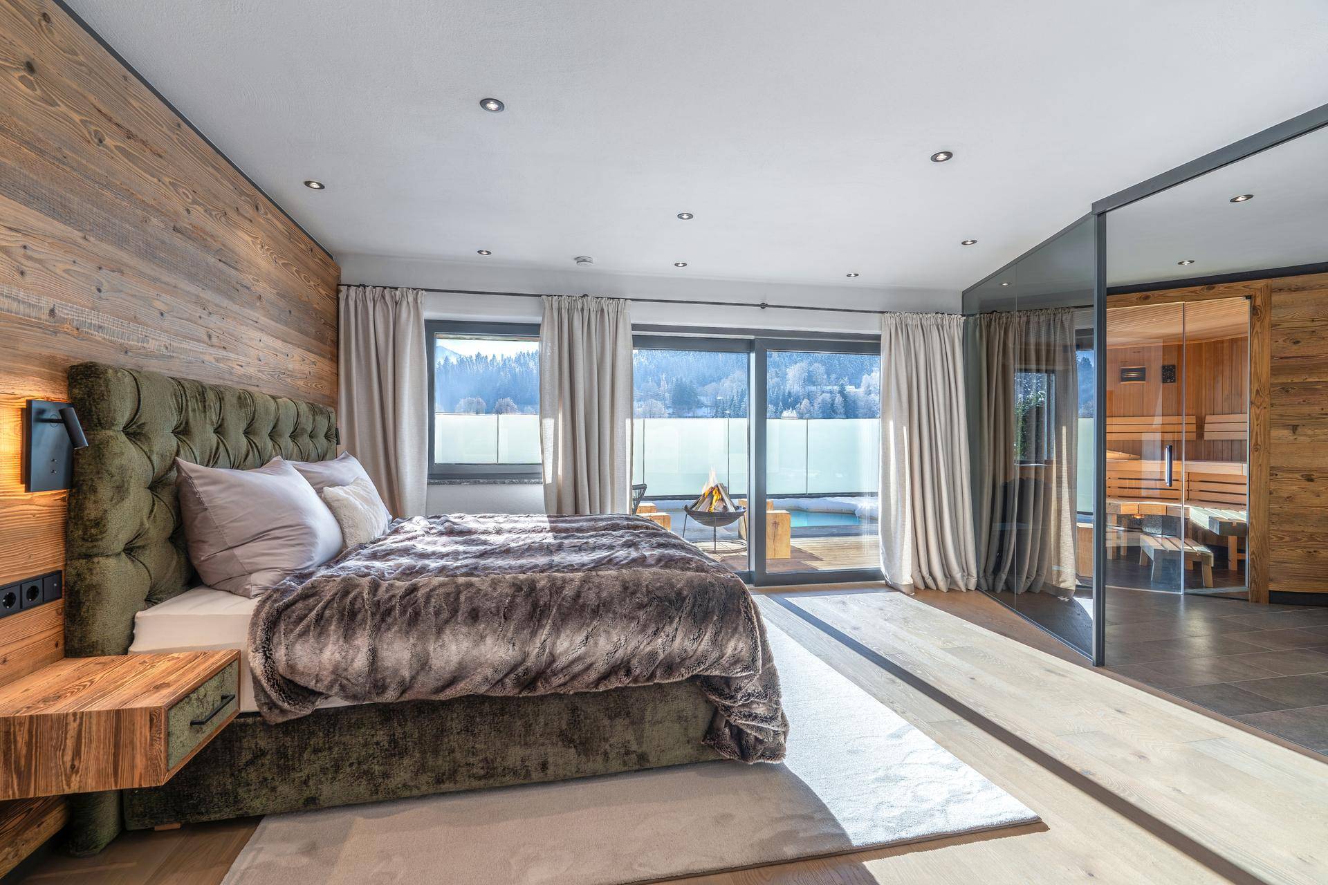 Elegantes Schlafzimmer mit Holzwand, großem Bett und direktem Zugang zu einer Sauna mit Bergblick.