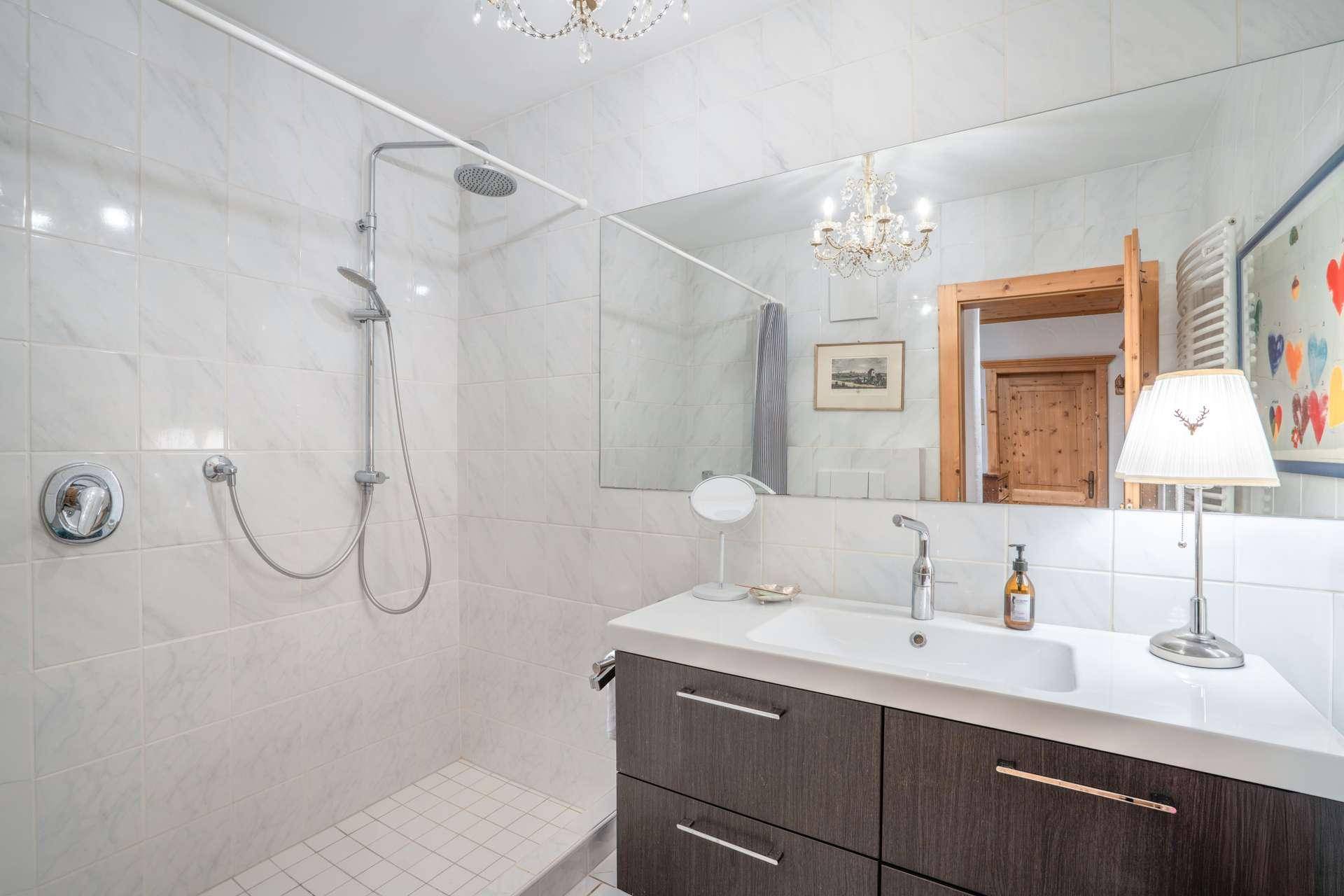 Modernes Badezimmer mit weißen Fliesen, großem Spiegel, Einzelwaschbecken und einer geräumigen Dusche.