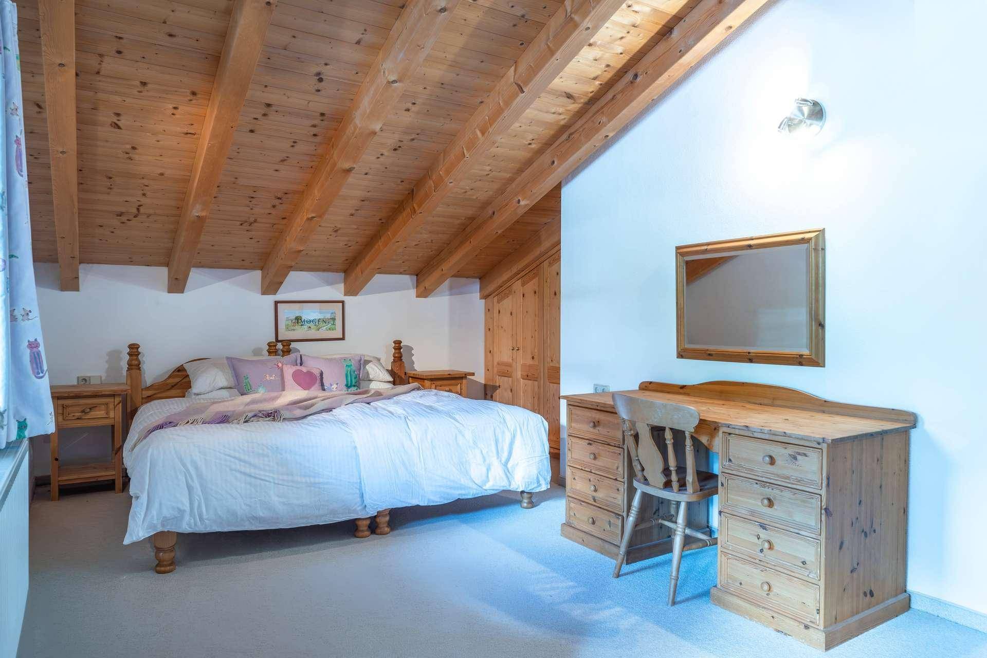 Schlafzimmer im Dachgeschoss mit sichtbaren Holzbalken, Doppelbett und rustikalen Holzmöbeln.