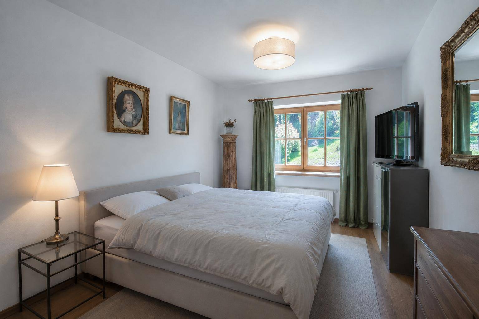 Gemütliches Schlafzimmer mit Doppelbett, Holzboden und Blick ins Grüne durch das Fenster.