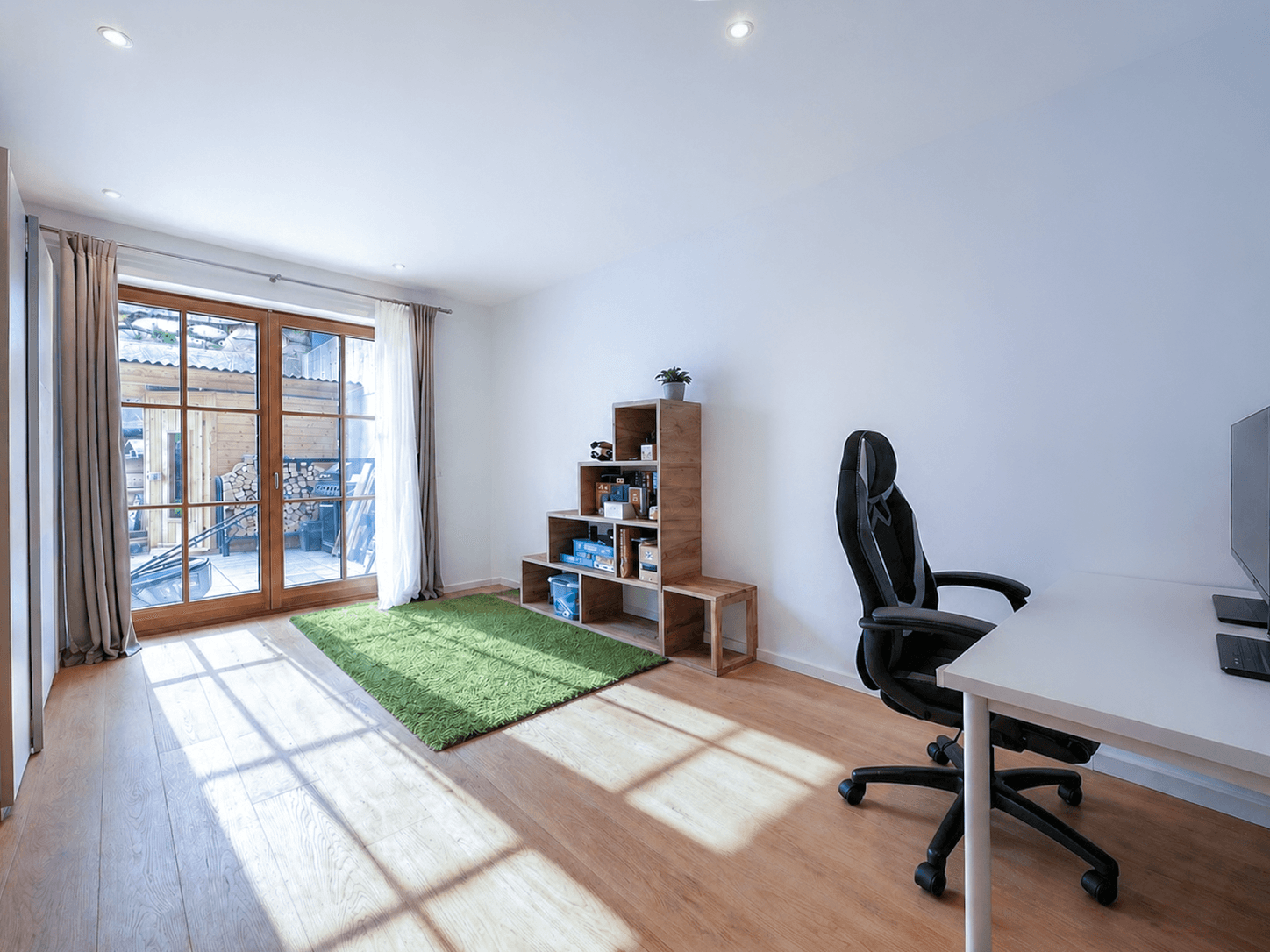 Helles Arbeitszimmer mit Holzboden, Schreibtisch und Zugang zu einem Außenbereich mit Holzstapel.
