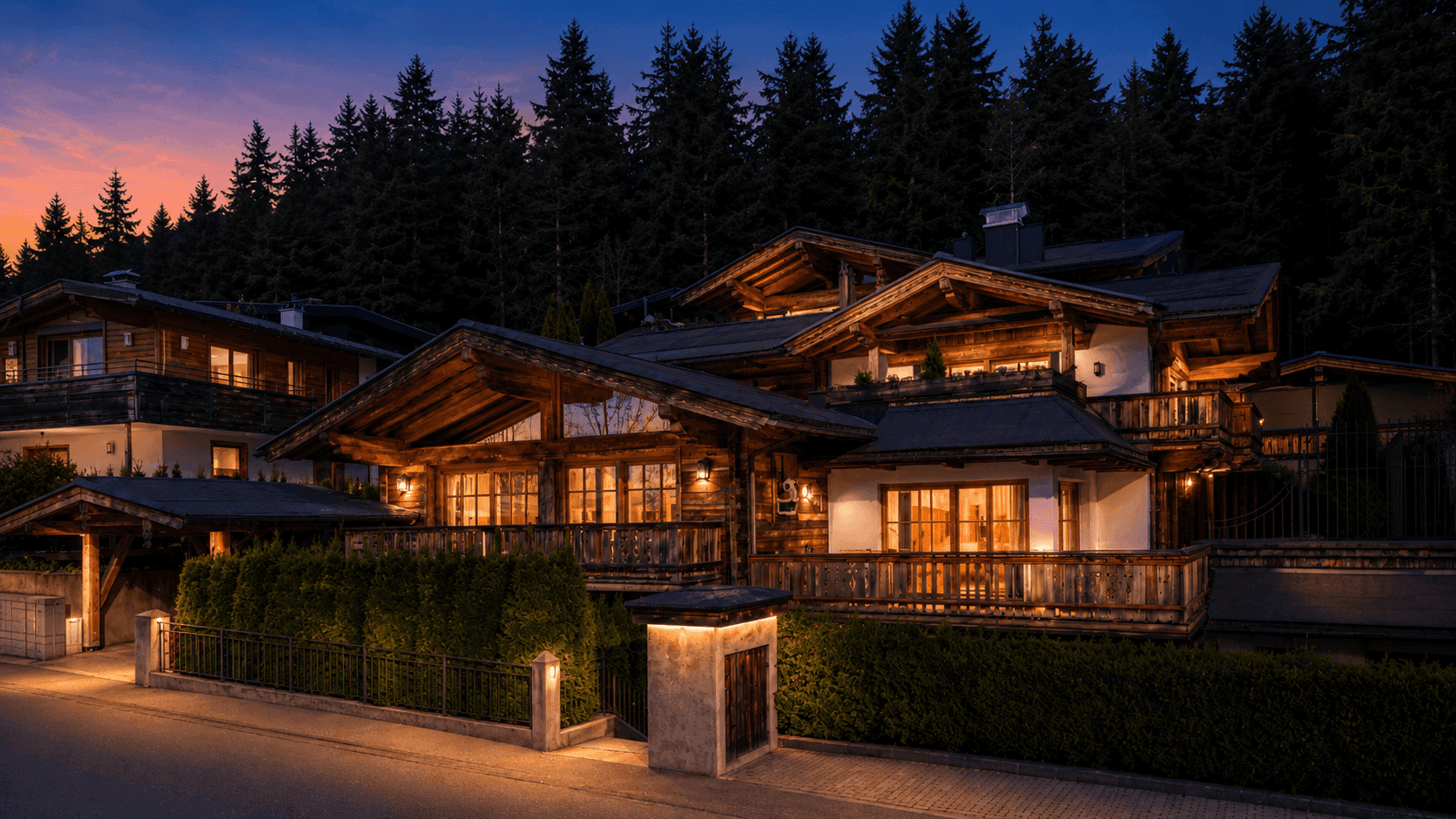 Luxuriöses Chalet im alpinen Stil bei Sonnenuntergang, umgeben von Wald und beleuchtet.