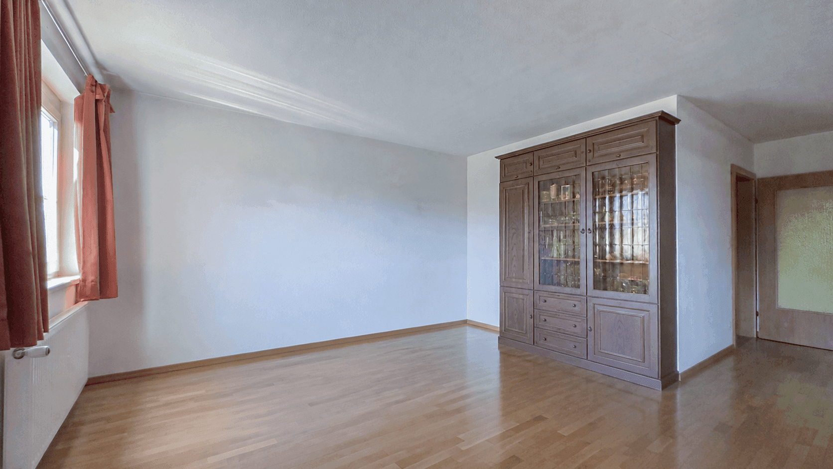 Geräumiger, heller Wohnraum mit Parkettboden und einem großen, eleganten Holzschrank.