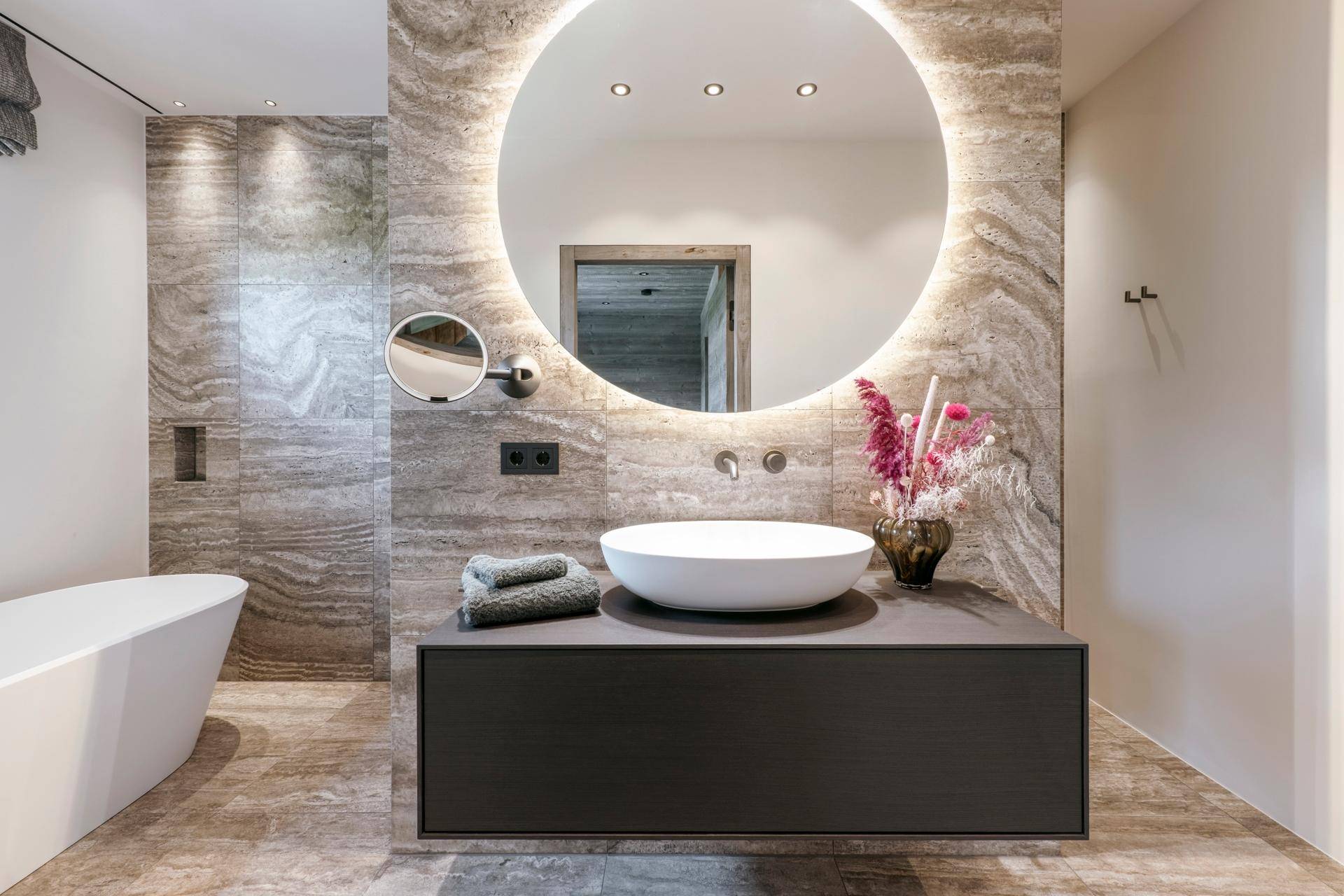 Elegantes Badezimmer mit großem beleuchtetem Spiegel, modernem Waschtisch und Natursteinwand.