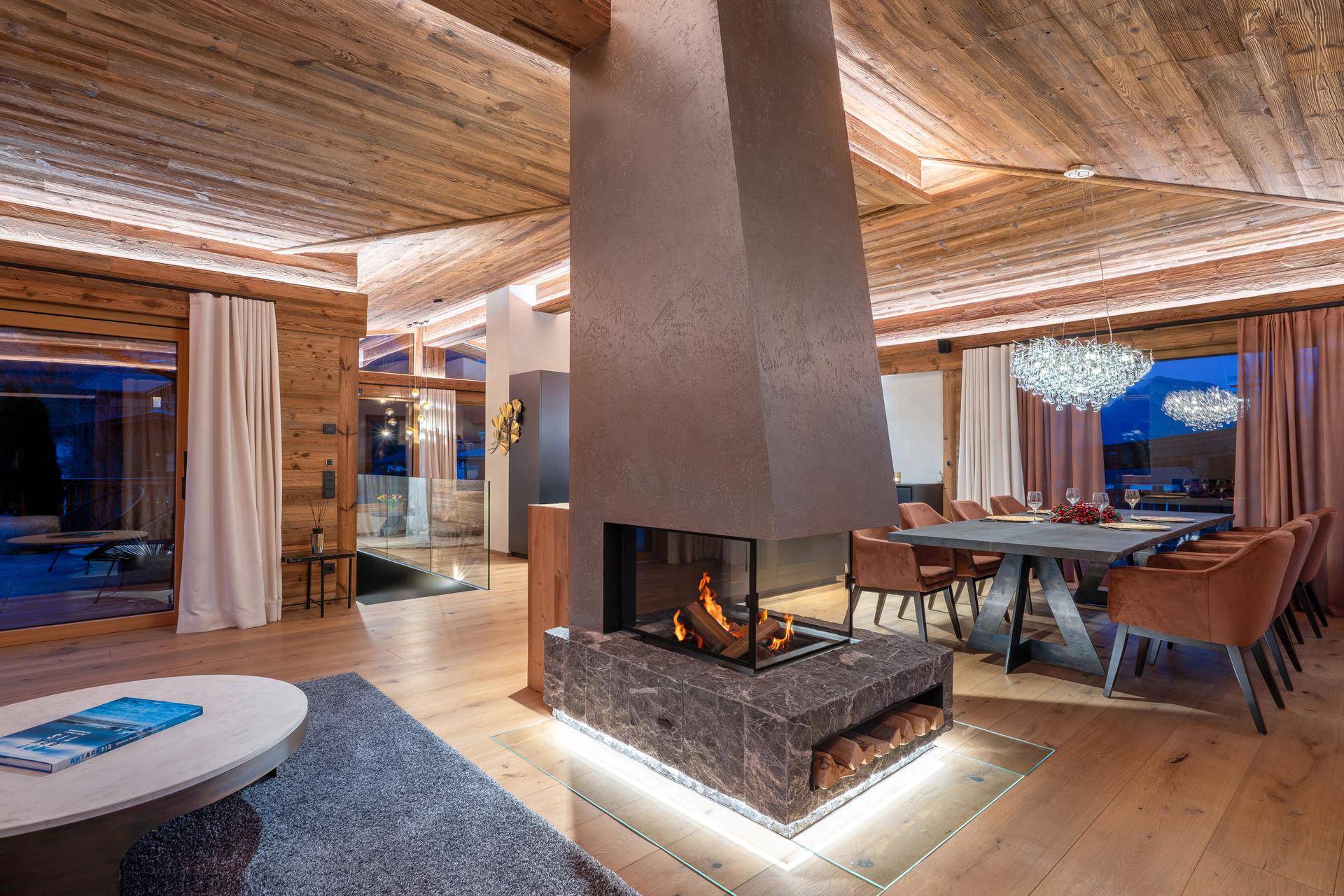Luxuriöser Wohn-Essbereich mit modernem Kamin, Holzbalkendecke und elegantem Kronleuchter.