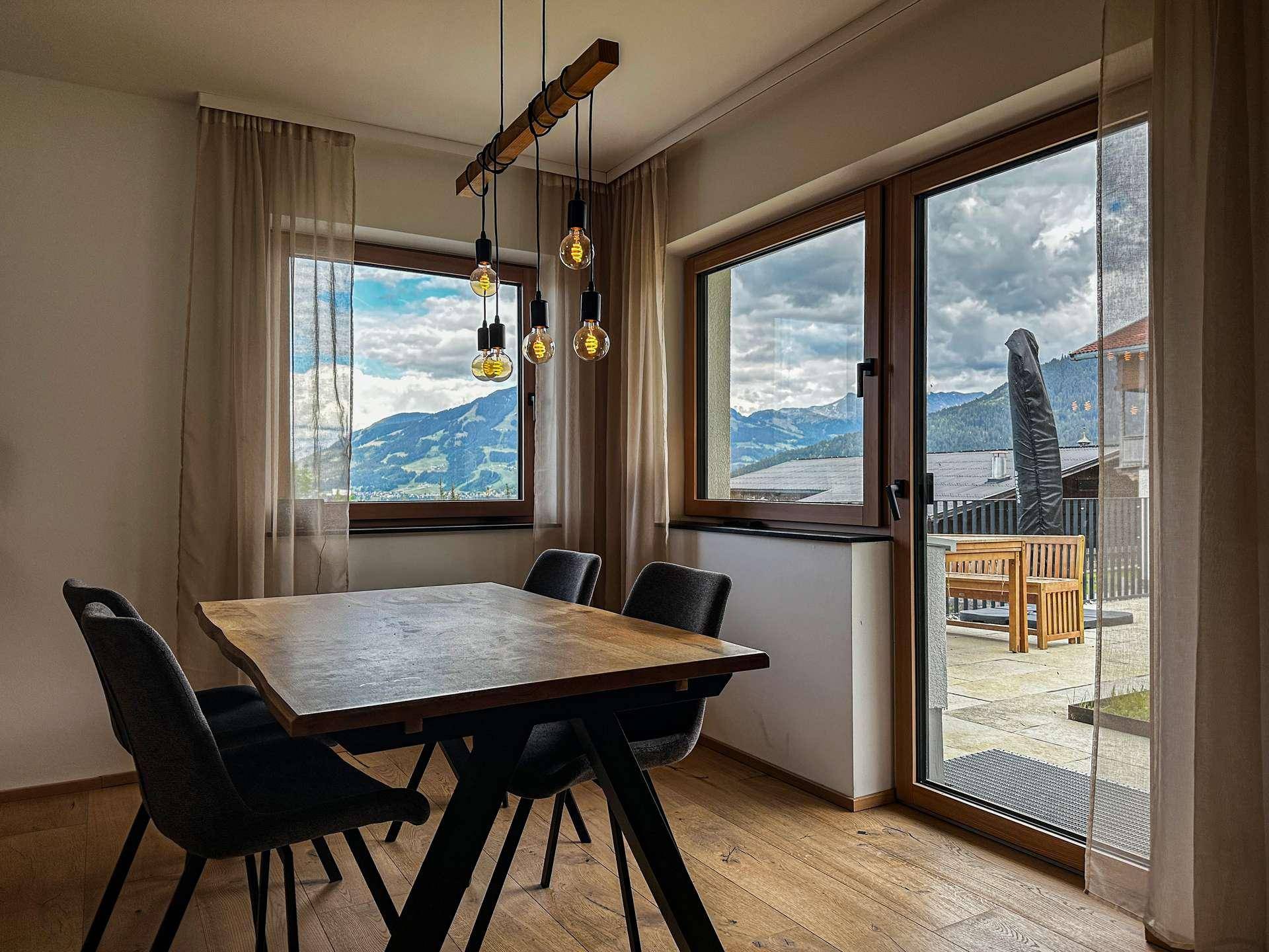 Heller Essbereich mit Holztisch, modernen Hängelampen und weitem Bergblick durch große Fenster.