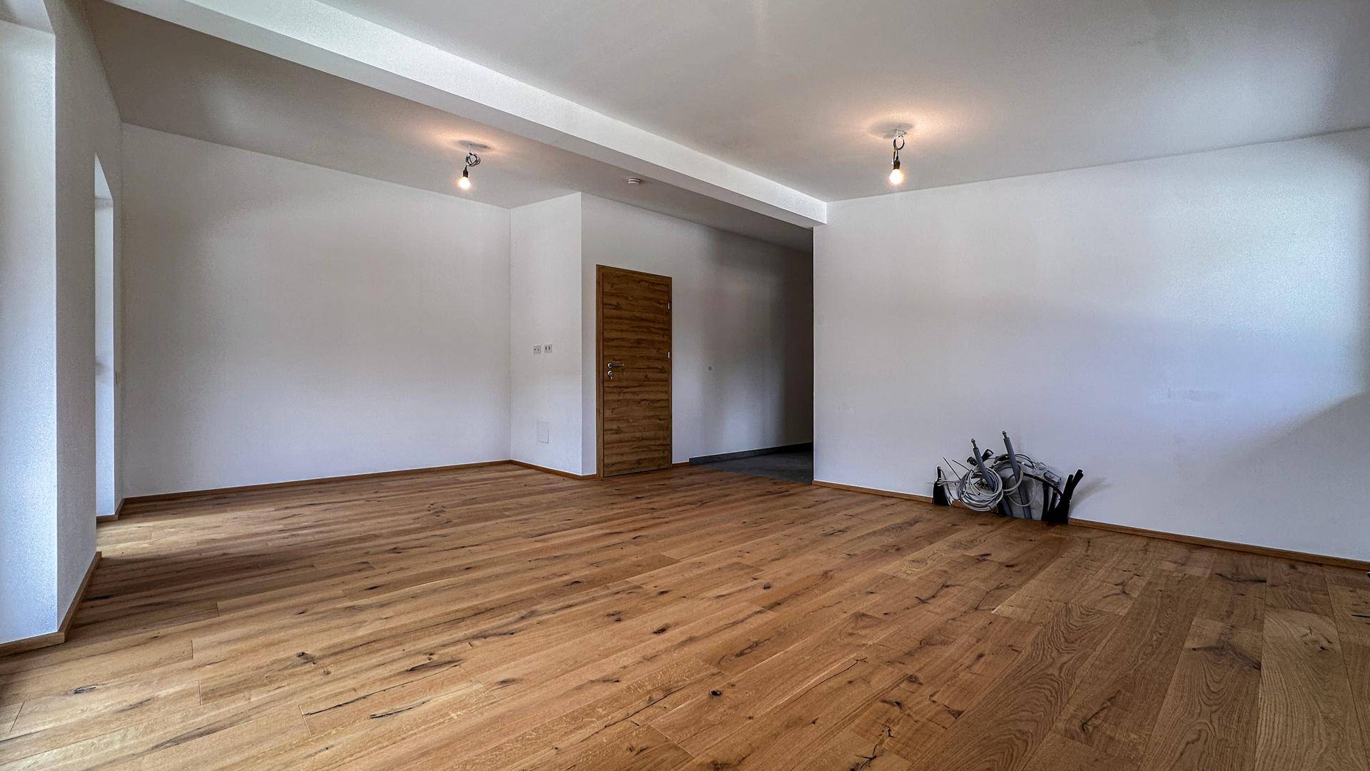 Heller, leerer Raum mit hochwertigem Holzboden und weiß gestrichenen Wänden.