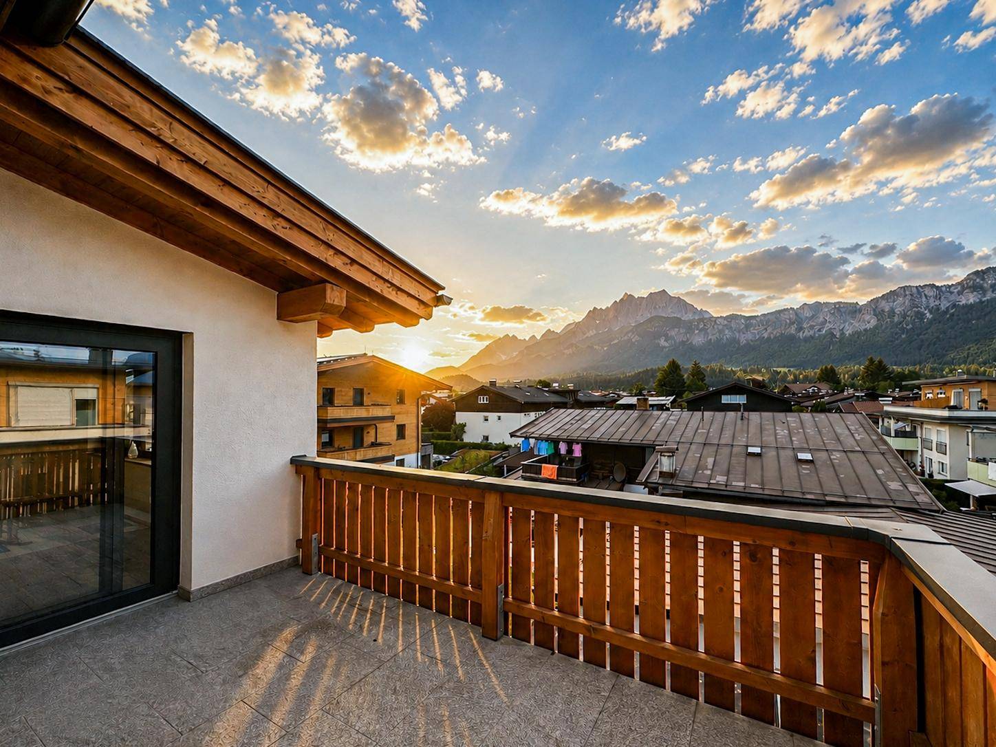 Balkon mit Fliesenboden und Holzgeländer, bietet einen malerischen Blick über die Stadt und Berge bei Sonnenuntergang.