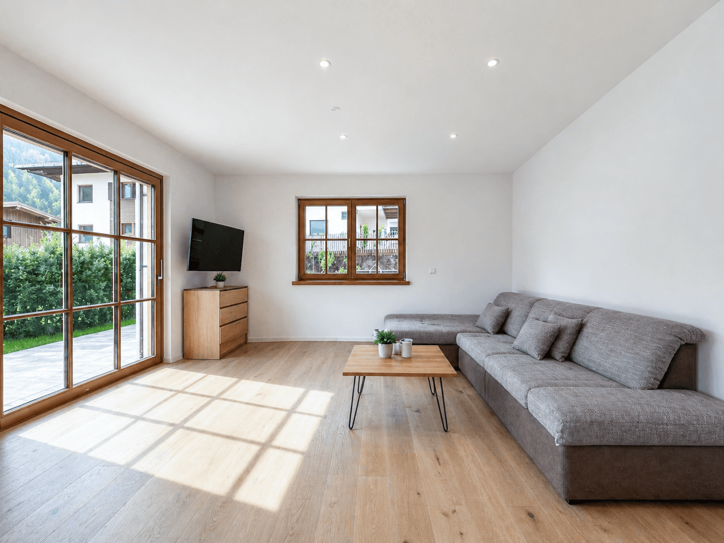 Helles Wohnzimmer mit großem Sofa, Holzboden und Zugang zur Terrasse mit Gartenblick.
