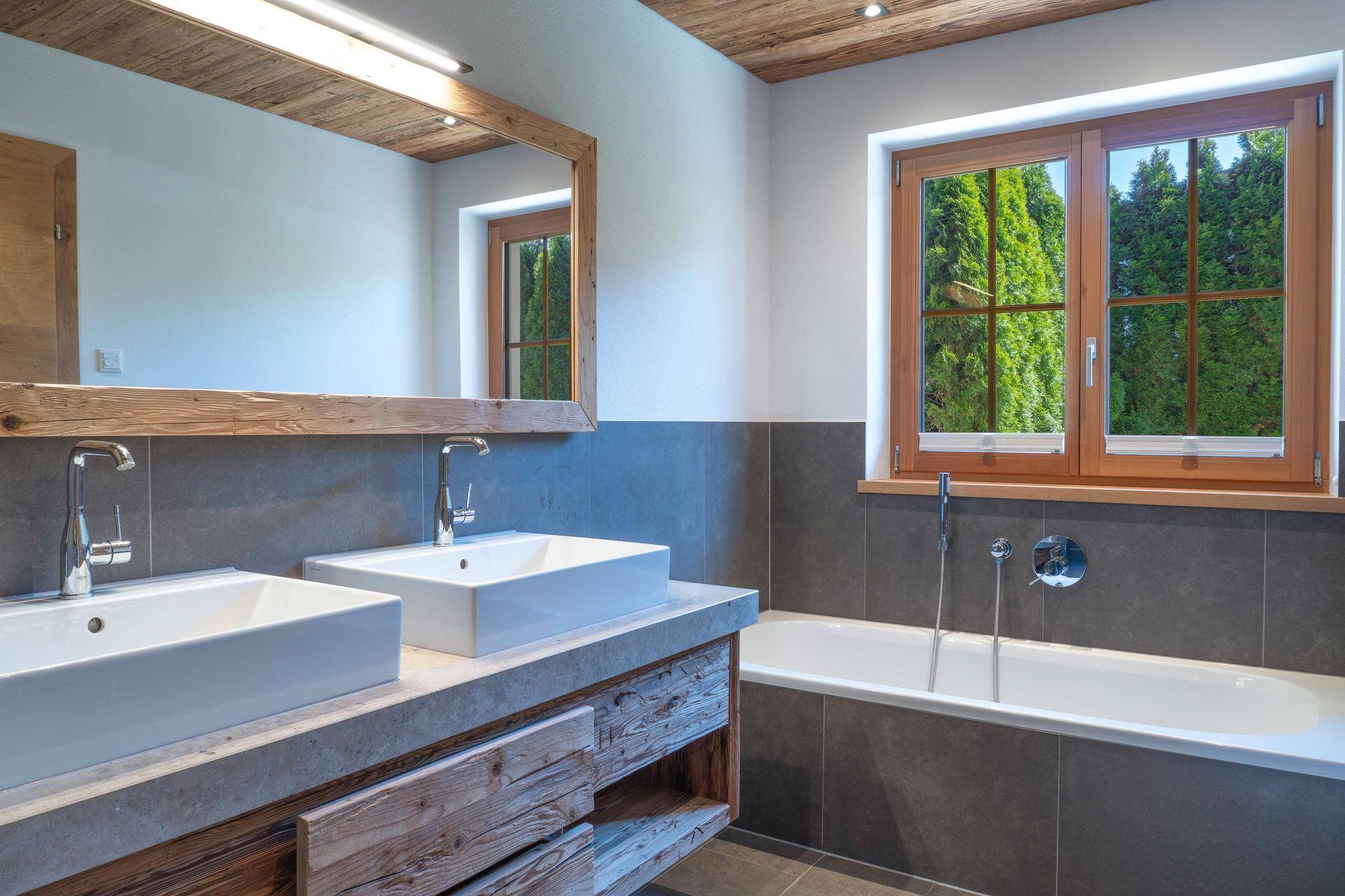 Modernes Badezimmer mit Doppelwaschbecken, Badewanne und Fenster mit Blick ins Grüne.