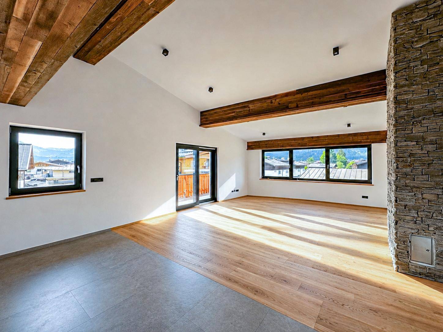 Offener Wohnraum mit Holzbalken, Steinwand, Parkettboden und Fliesenbereich sowie Bergblick.