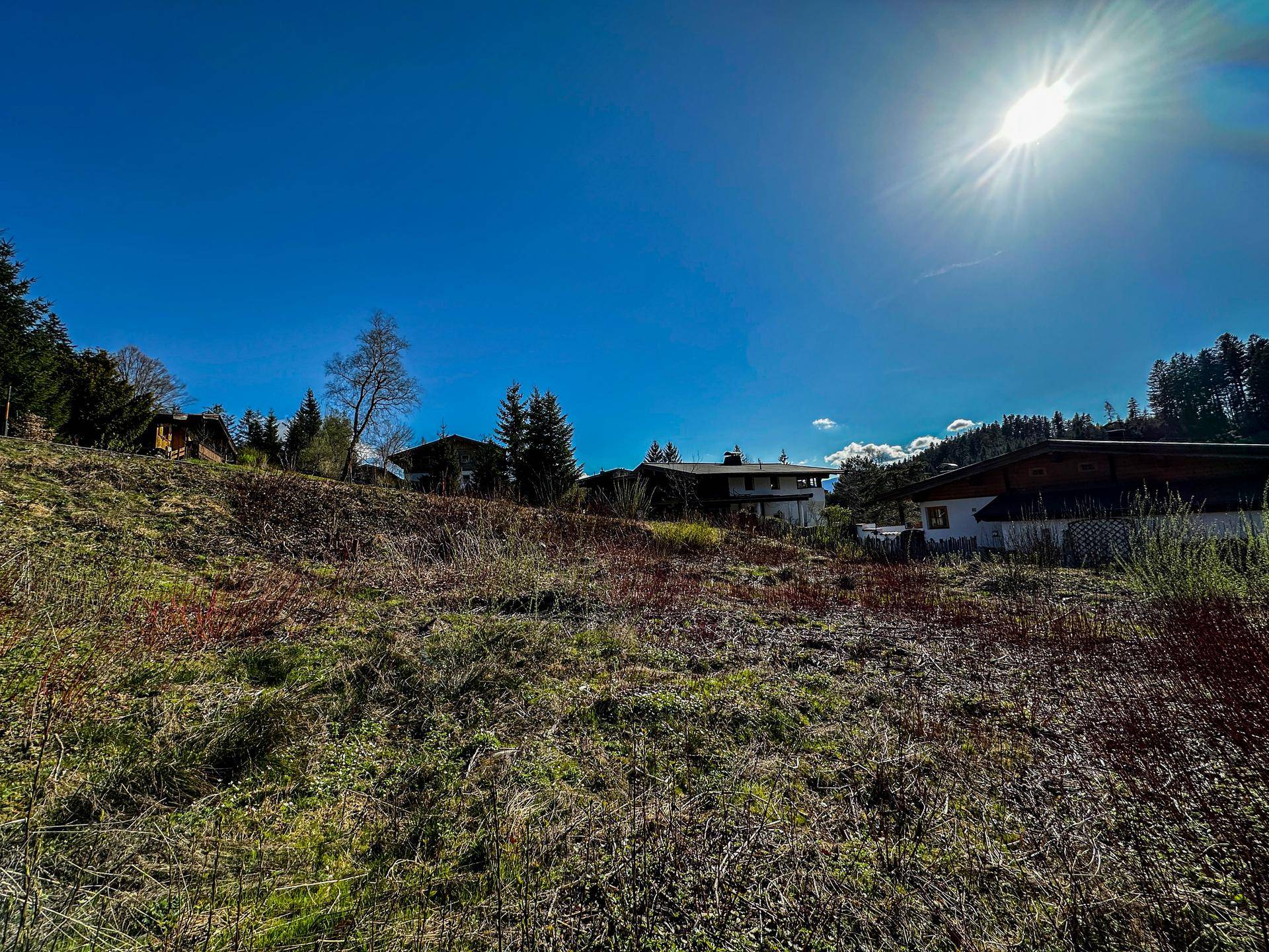 Weitläufige grüne Landschaft mit Häusern, Wiesen und einem sonnigen blauen Himmel über den Hügeln.