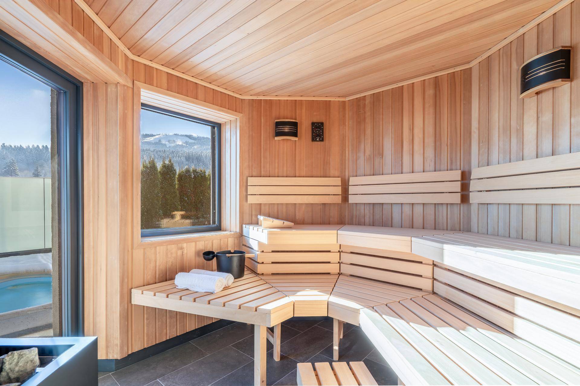 Geräumige Holzsauna mit Blick auf die verschneite Landschaft und Zugang zu einem Whirlpool im Freien.
