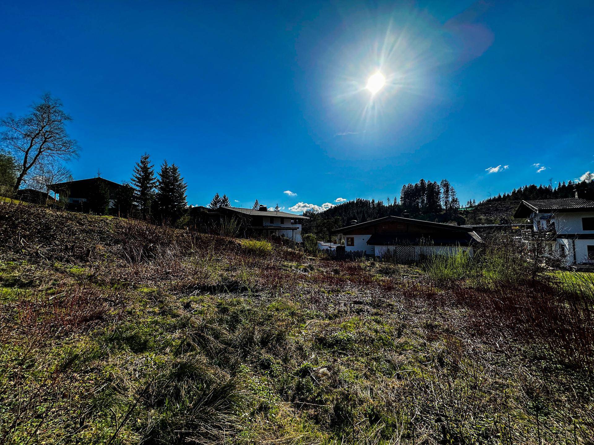 Sonnige Landschaft mit traditionellen Häusern, grünen Hügeln und einem strahlend blauen Himmel.