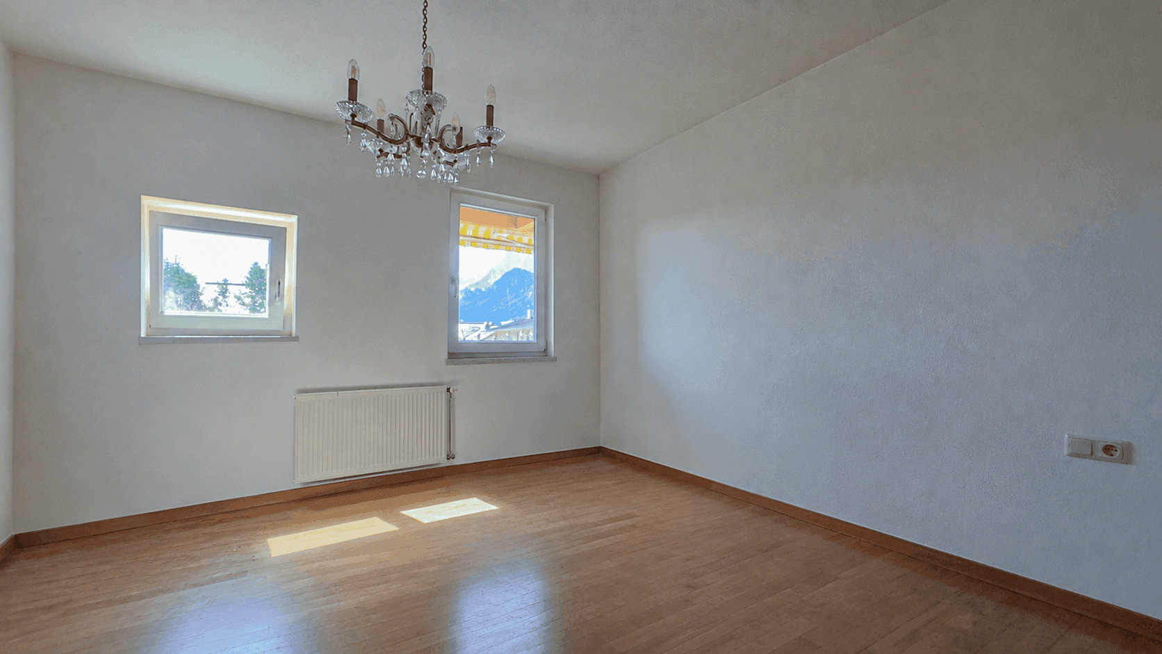 Helles Zimmer mit Parkettboden, Kronleuchter und Blick auf die umliegende Berglandschaft.