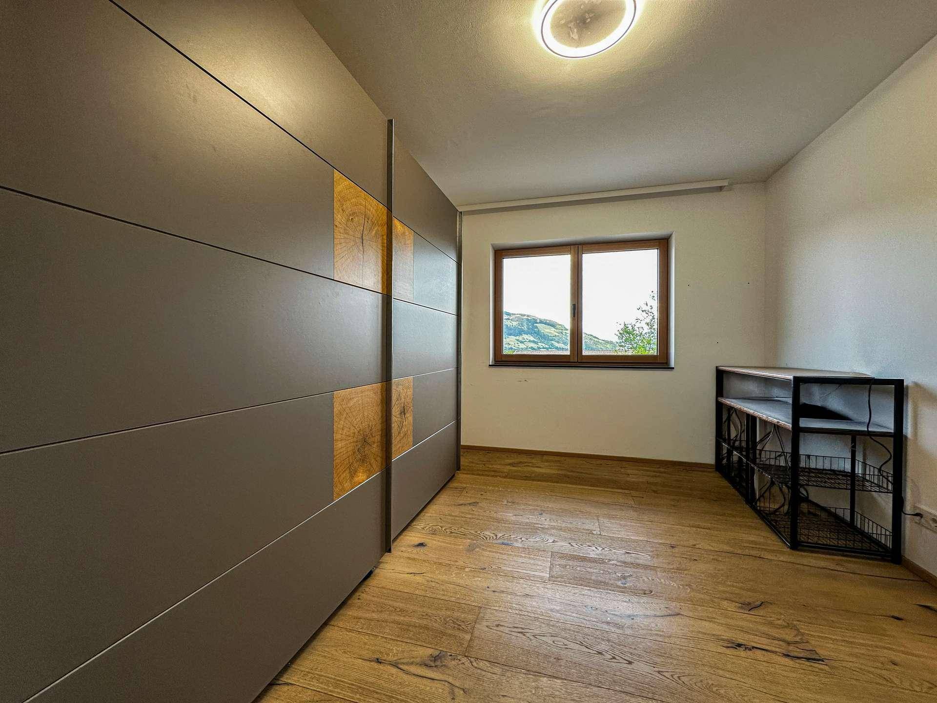 Geräumiges Schlafzimmer mit Holzboden, großem Kleiderschrank und Fenster mit Bergblick.