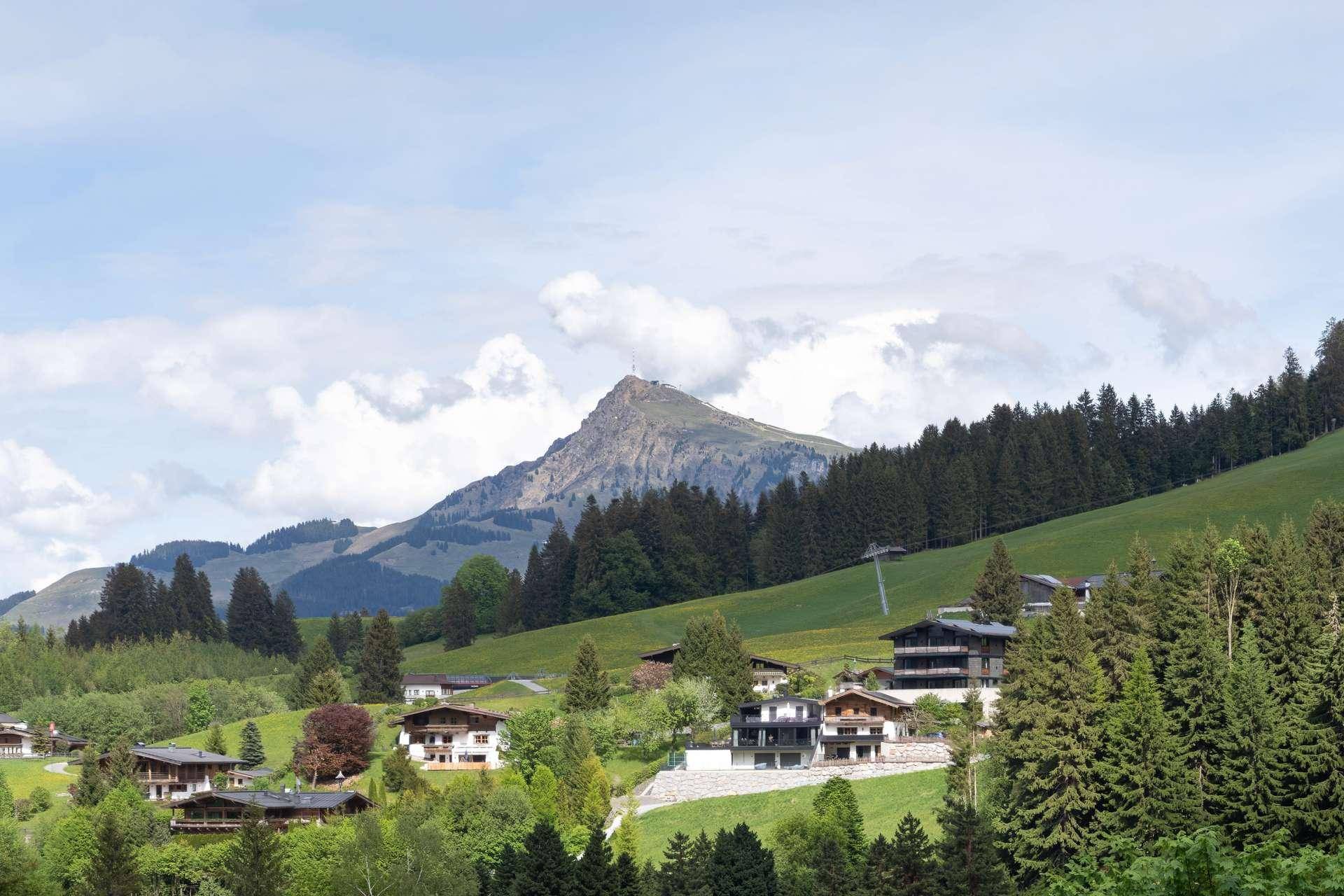 Malerische Berglandschaft mit verstreuten Häusern und üppigen grünen Wäldern unter blauem Himmel.