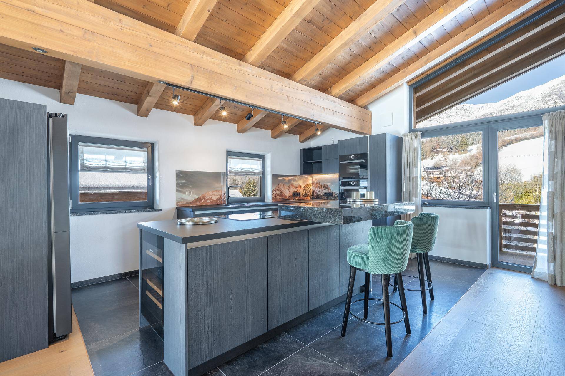 Moderne Küche mit dunklen Schränken, Kücheninsel und Bergblick durch große Fenster.