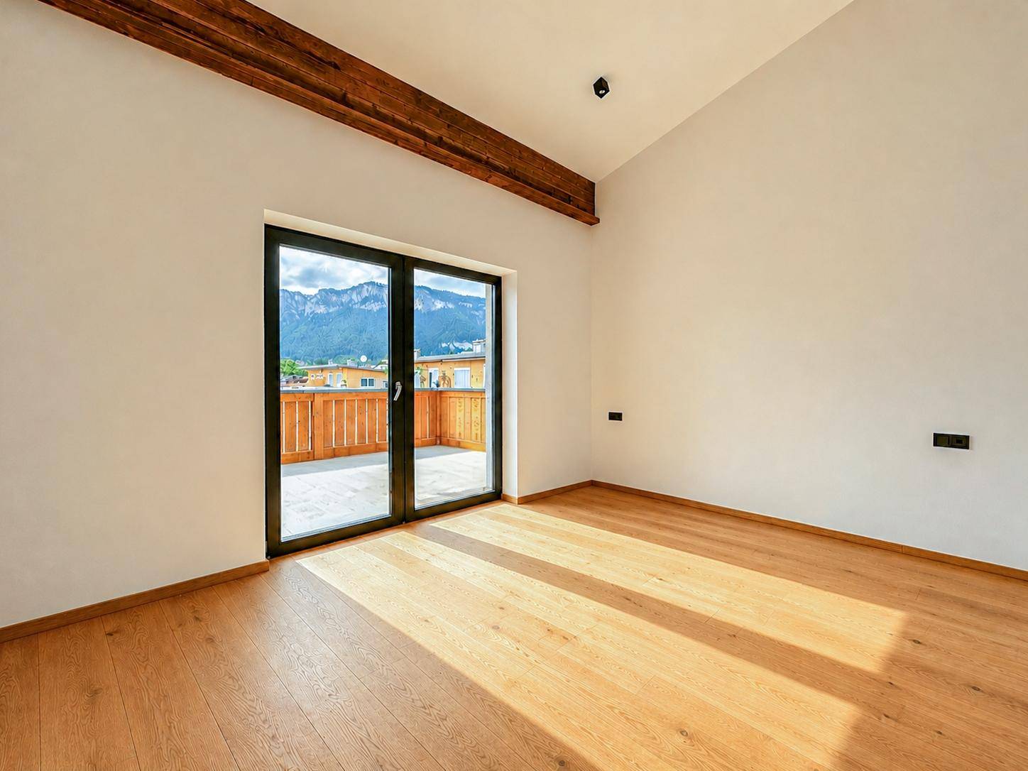 Lichtdurchfluteter Raum mit Holzboden, Balkonzugang und beeindruckendem Bergblick.