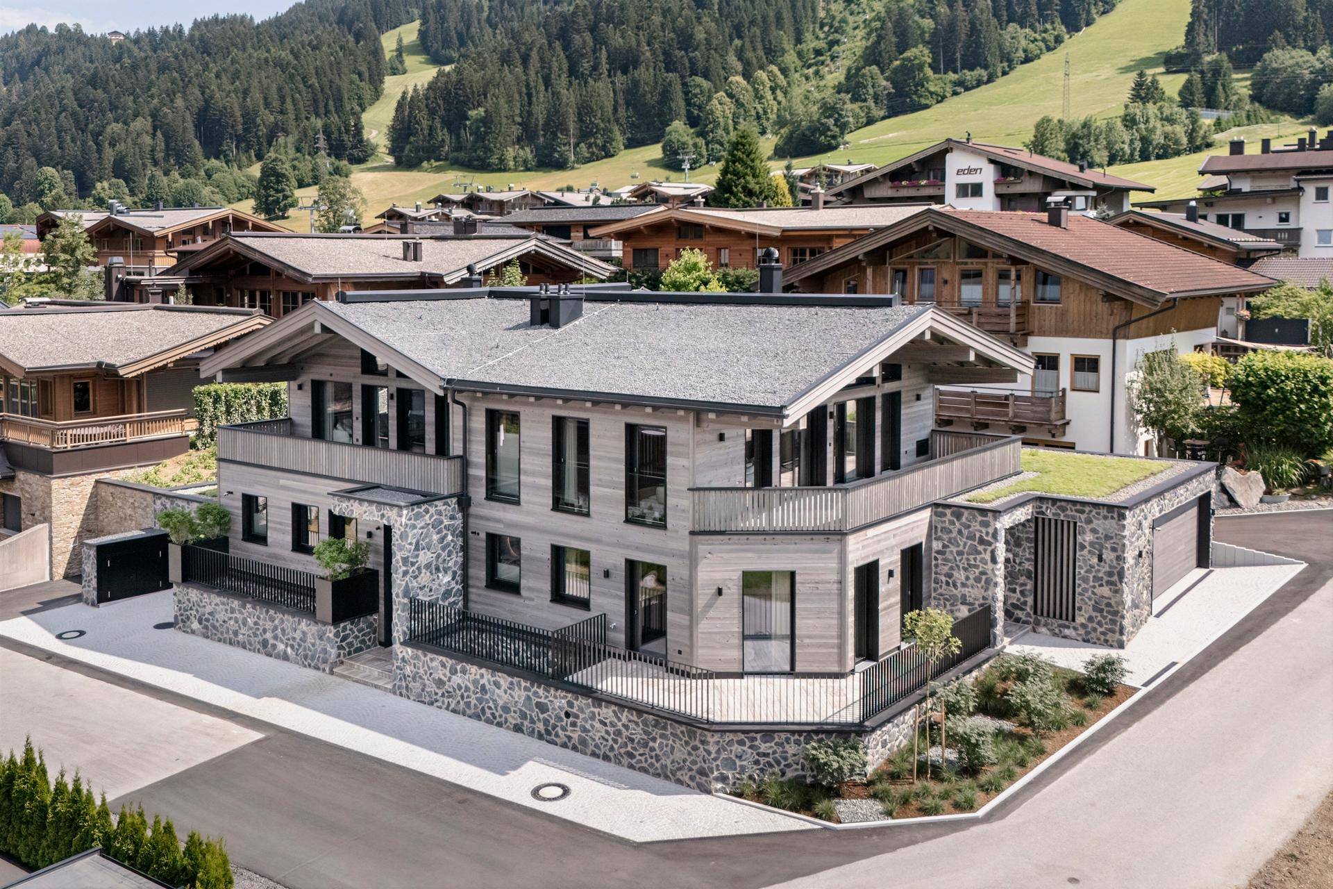 Luxuriöses Chalet mit Steinfassade, Balkonen und Gründach in einer malerischen Berglandschaft.