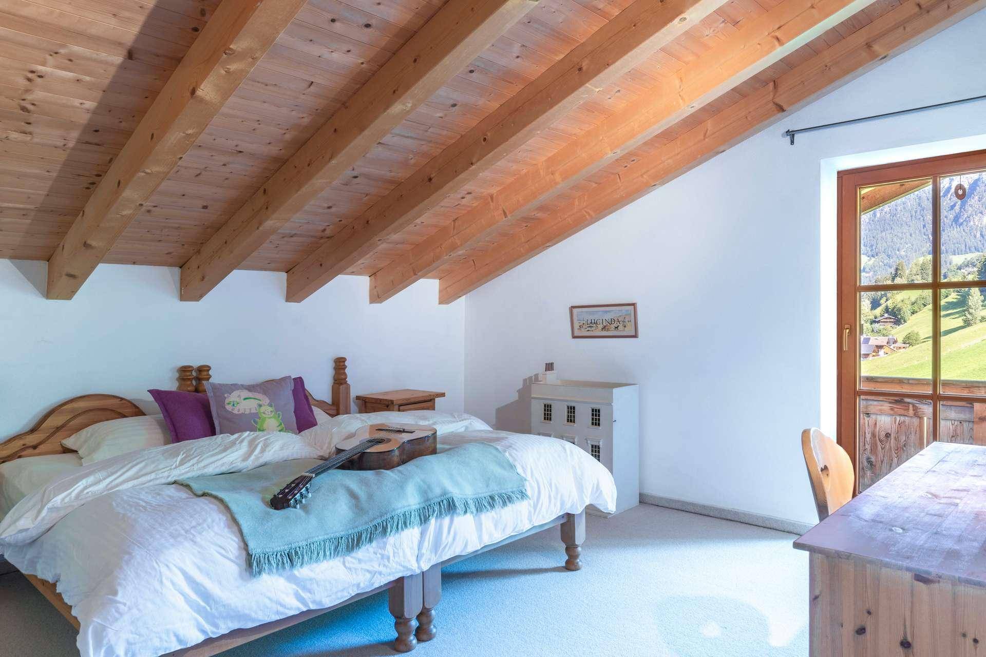 Helles Schlafzimmer mit Holzbalkendecke, Doppelbett und Zugang zu einem Balkon mit Bergblick.
