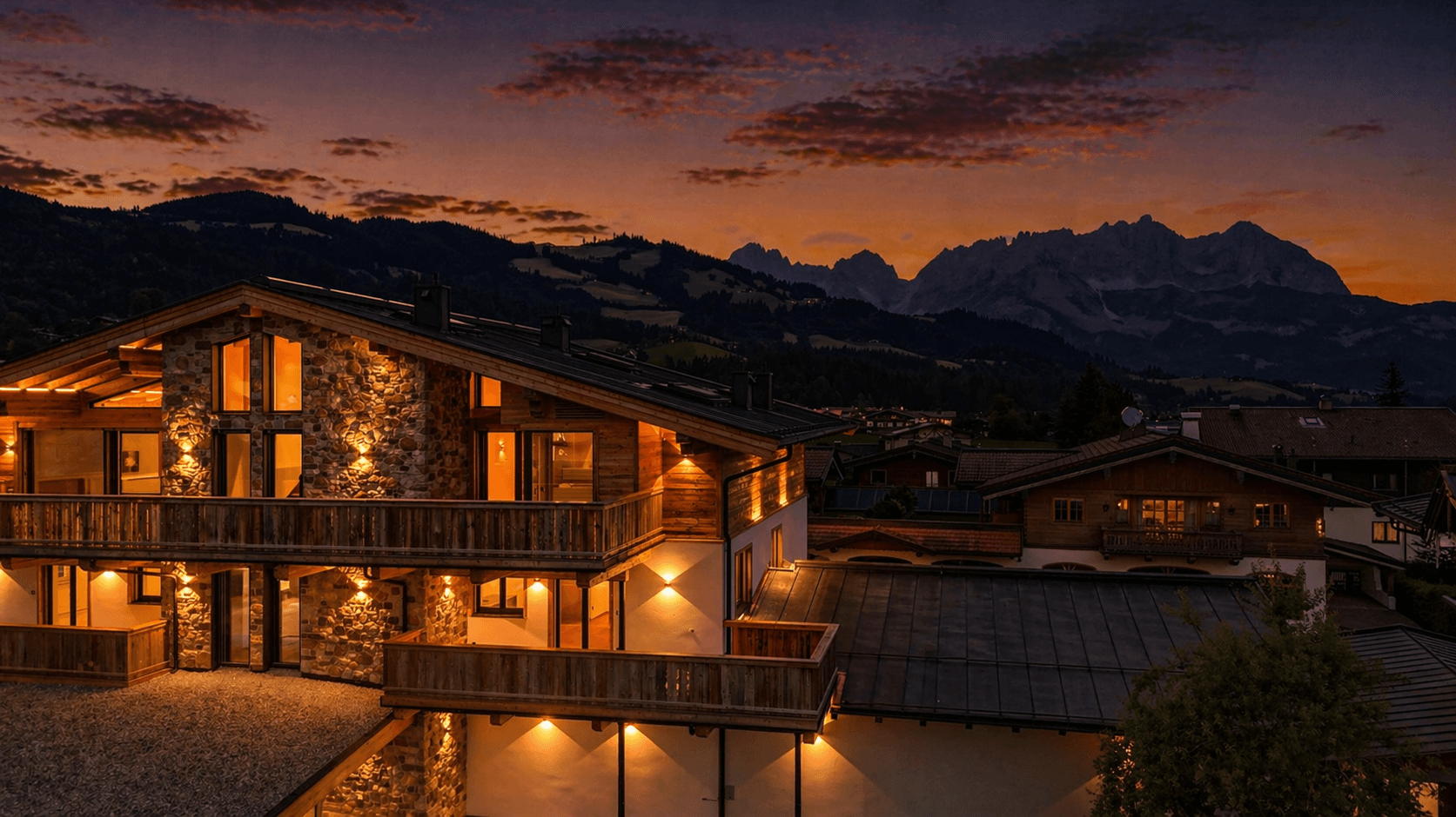 Luxuriöses Chalet im alpinen Stil mit beleuchteter Fassade und Bergblick bei Nacht.