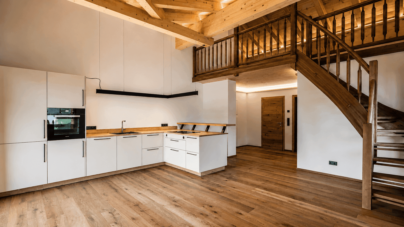 Offener Wohnbereich mit moderner Einbauküche, Holzbalken und Treppe zur Galerie.