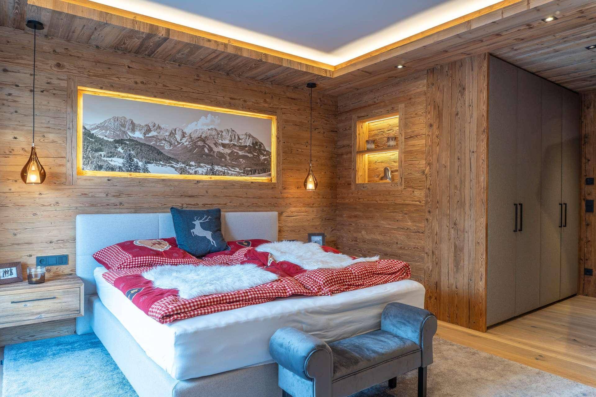 Gemütliches Schlafzimmer im alpinen Stil mit Holzwänden, Deckenbeleuchtung und großem Bett.