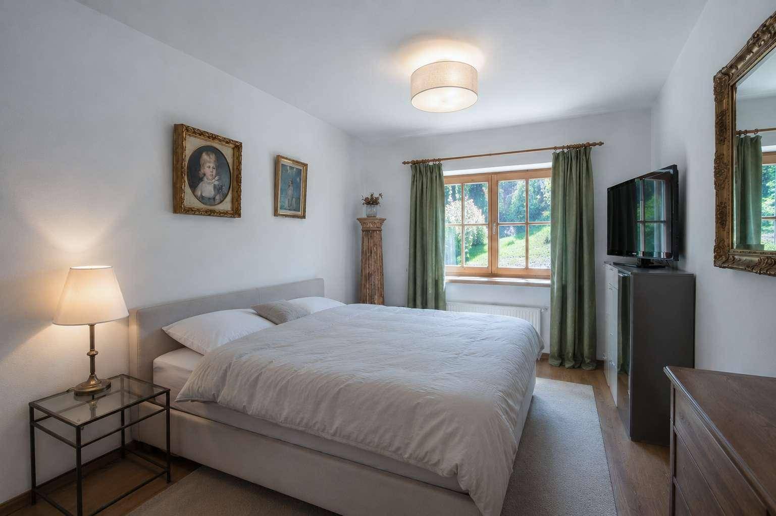Ruhiges Schlafzimmer mit Doppelbett, Holzboden und einem Fenster mit Blick ins Grüne.