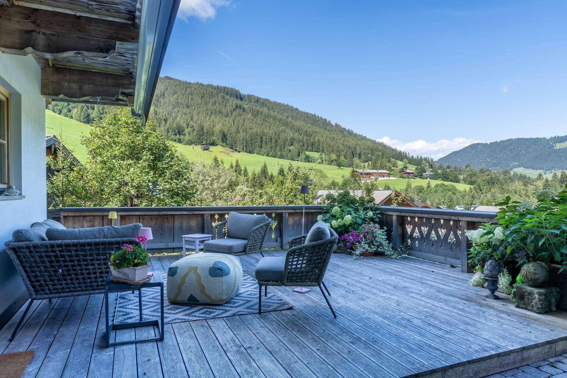 Geräumige Holzterrasse mit bequemen Lounge-Möbeln und weitem Blick auf die umliegende Bergwelt.