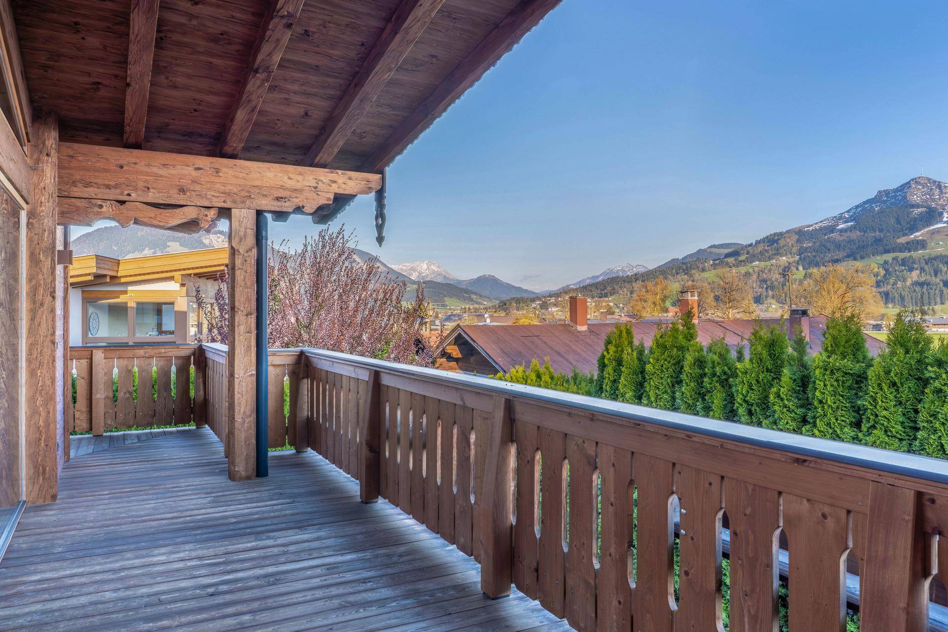 Großer überdachter Balkon mit Holzboden und Geländer, bietet weiten Bergblick.