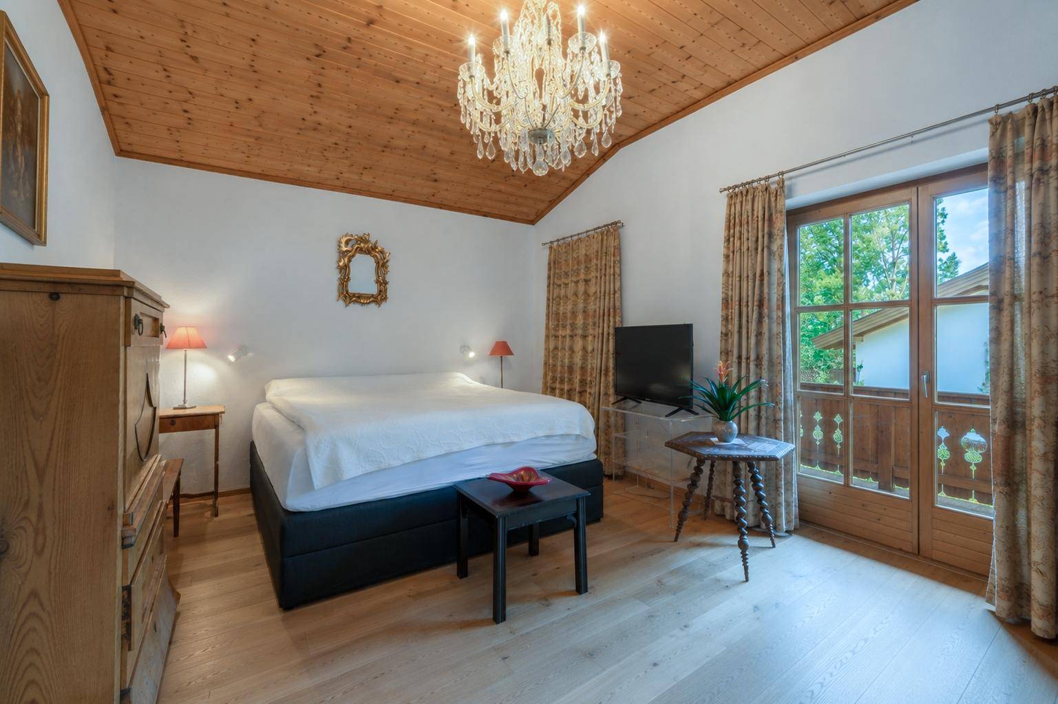 Geräumiges Schlafzimmer mit Holzbalkendecke, Kronleuchter und Zugang zum Balkon.