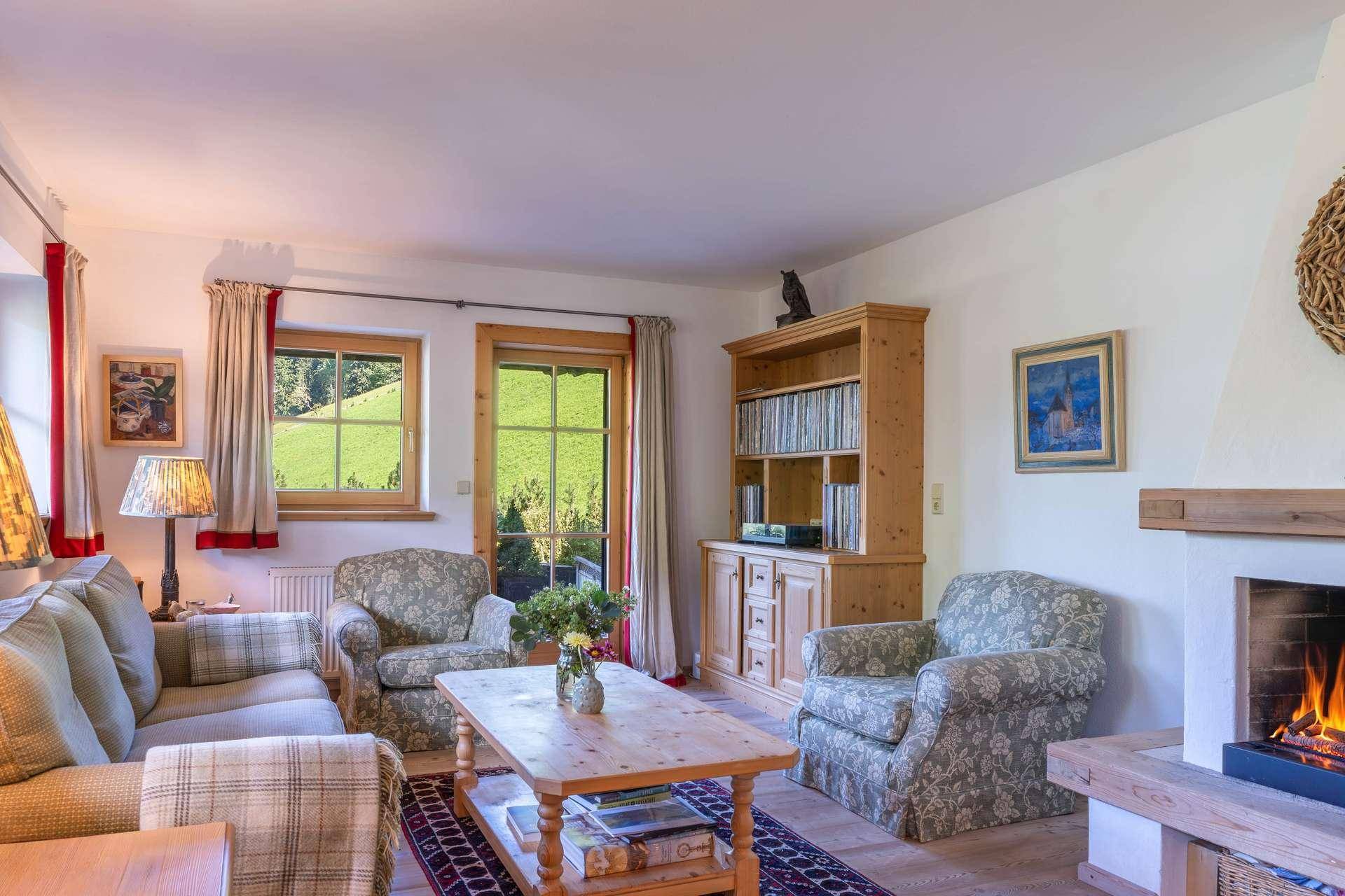 Gemütliches Wohnzimmer mit Kamin, bequemen Sofas und Blick auf die grüne Berglandschaft.