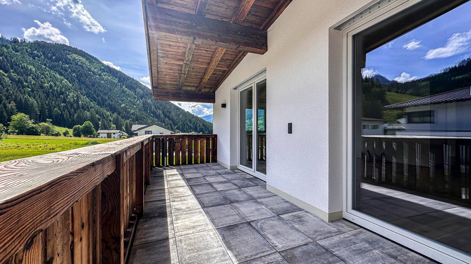 Geräumiger Balkon mit Holzbalken, Fliesenboden und einem atemberaubenden Blick auf die umliegenden Berge.