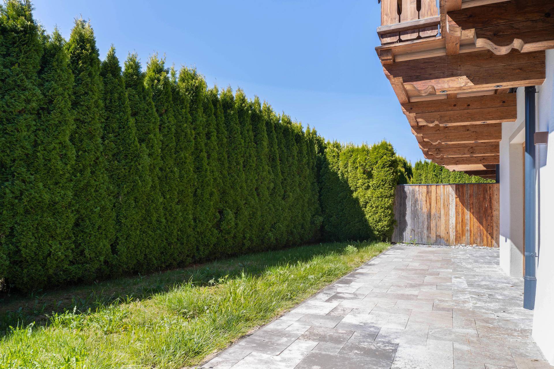 Gepflasterter Außenbereich mit Rasenfläche und hoher Hecke für Privatsphäre.